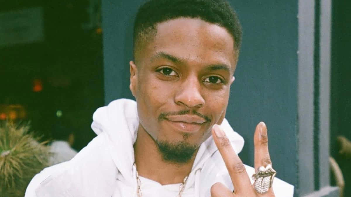 Pierre Bourne 桌布 壁紙 — 一位身穿白色連帽衫的年輕男子微笑著，手指上戴著一個大戒指比出和平手勢。