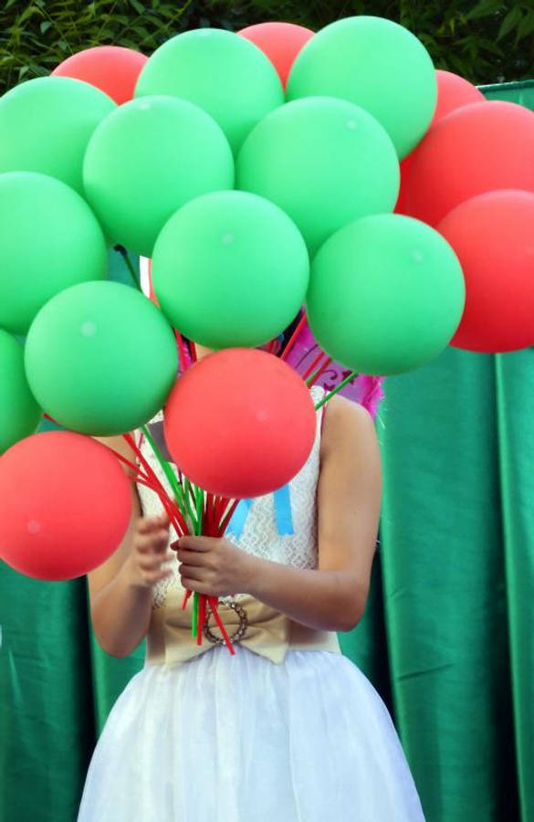 Balloons 桌布 壁紙 — 一位身穿白色連衣裙的人手持一束鮮豔的綠色和紅色氣球，遮住了他們的臉，背景是綠色窗簾。