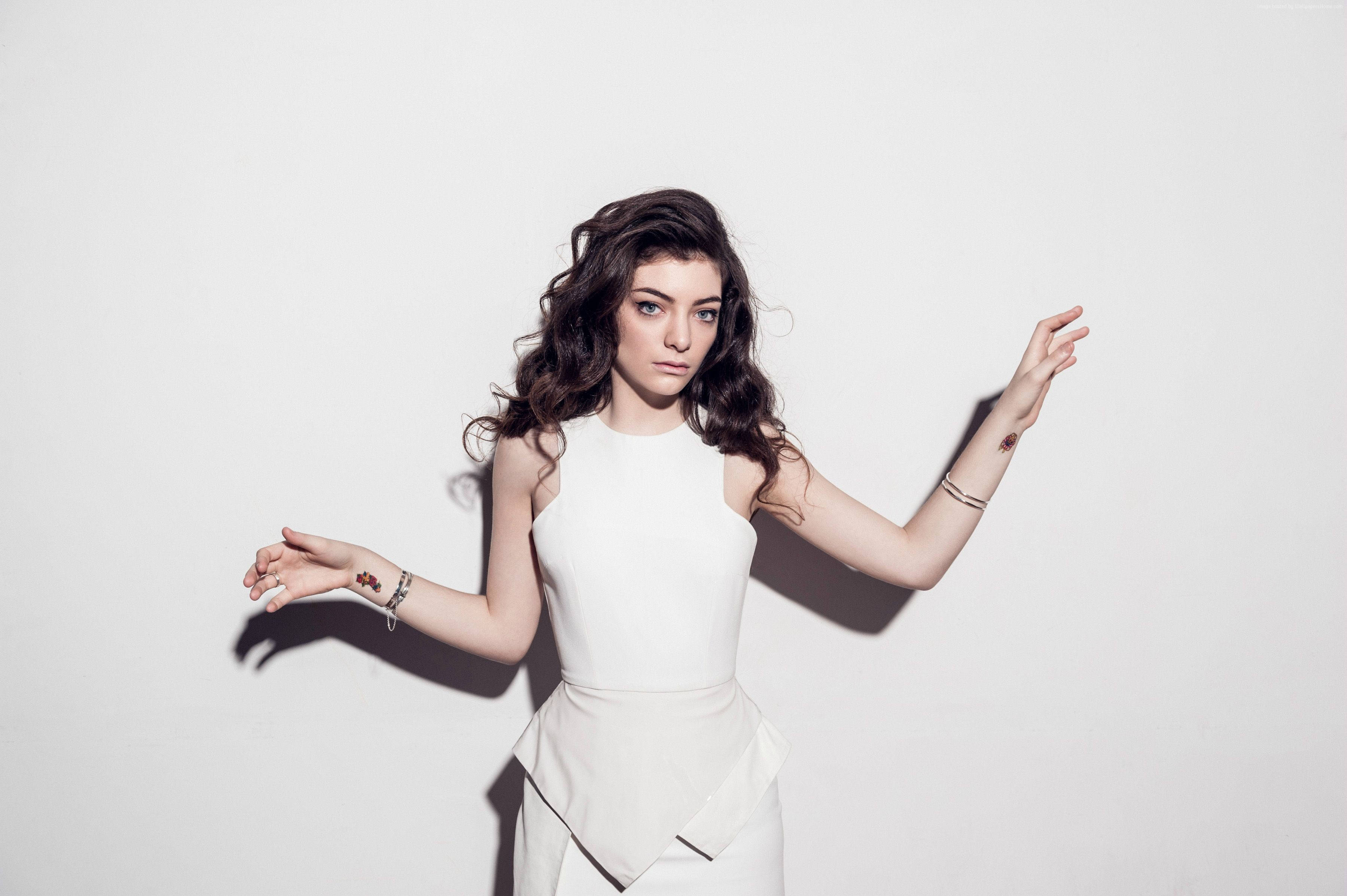 Lorde 桌布 壁紙 — 一位身穿白色連衣裙的女性在純白背景下張開雙臂擺姿勢，投射出戲劇性的陰影。