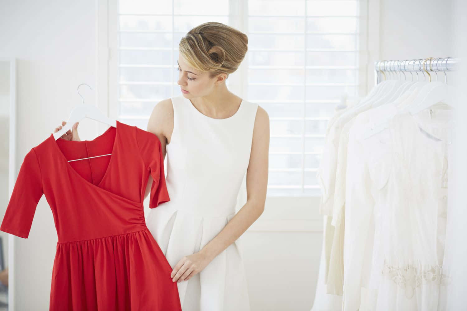 Red Clothing 桌布 壁紙 — 一位身穿白色連衣裙的女性正在明亮簡約的服裝精品店中檢查掛在衣架上的鮮紅色連衣裙。
