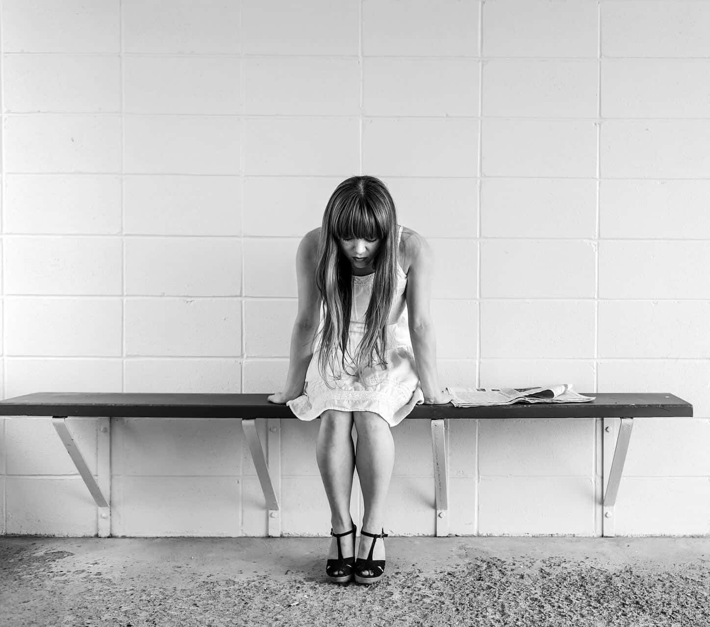 Alone 桌布 壁紙 — 一位身穿白色連衣裙的女性獨自坐在靠著瓷磚牆的長椅上，低頭沉思。