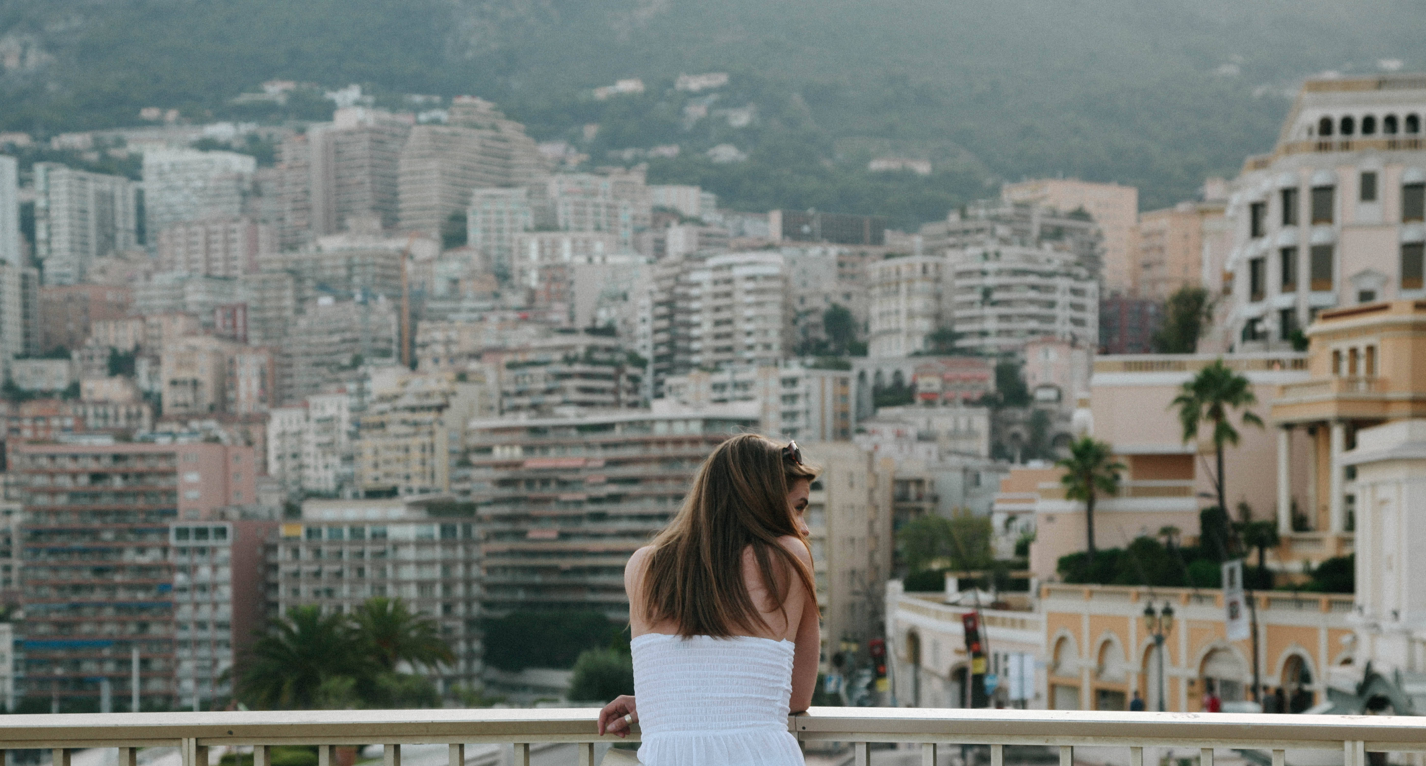 Monaco 桌布 壁紙 — 一位身穿白色連衣裙的女性眺望著一座坐落在綠丘之間、人口稠密的沿海城市。
