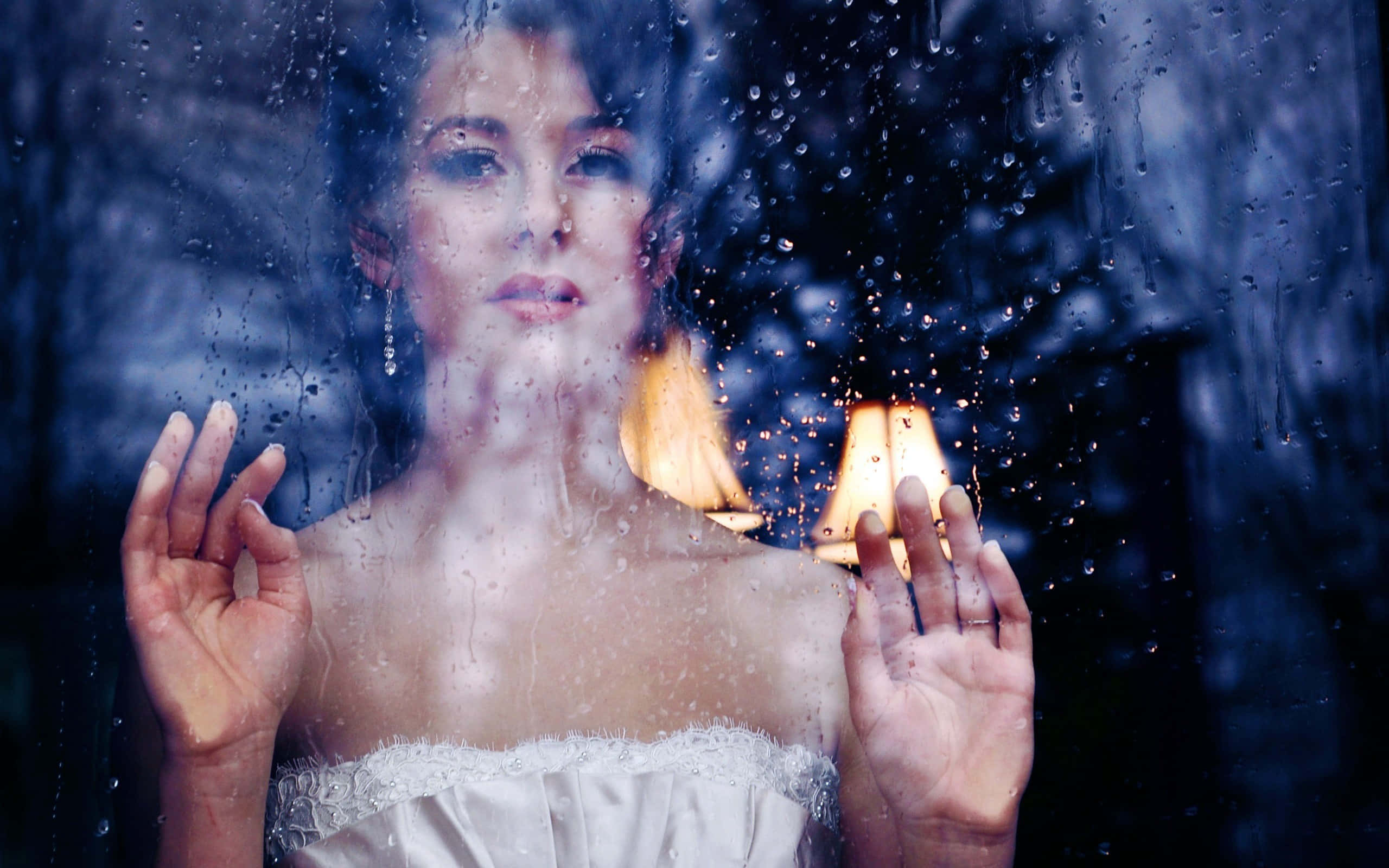Emotional 桌布 壁紙 — 一位身穿白色連衣裙的女性透過濺滿雨水的窗戶凝視，雙手按在玻璃上，身後一盞溫暖的燈在發光。
