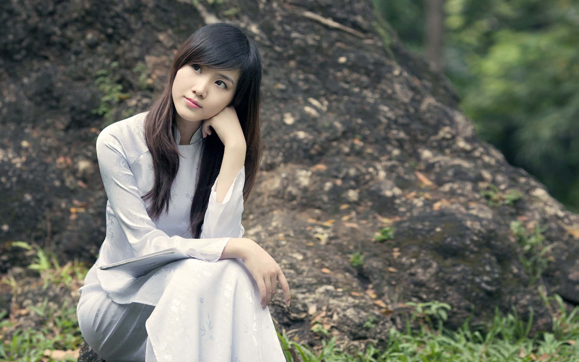Sitting Alone 桌布 壁紙 — 一位身穿白色連衣裙的年輕女子坐在長滿青苔的石頭上，周圍是鬱鬱蔥蔥的綠色森林。