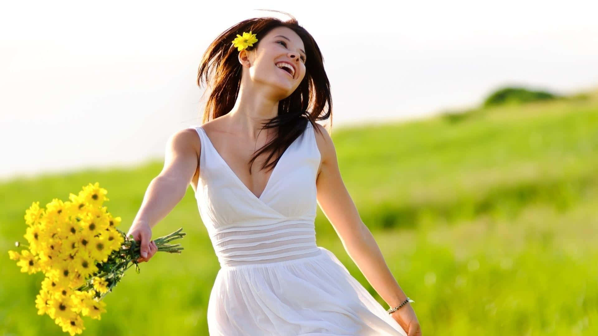 happiness 桌布 壁紙 — 一位身穿白色連衣裙的快樂女性在陽光明媚的綠色田野中手持黃色花朵大笑。