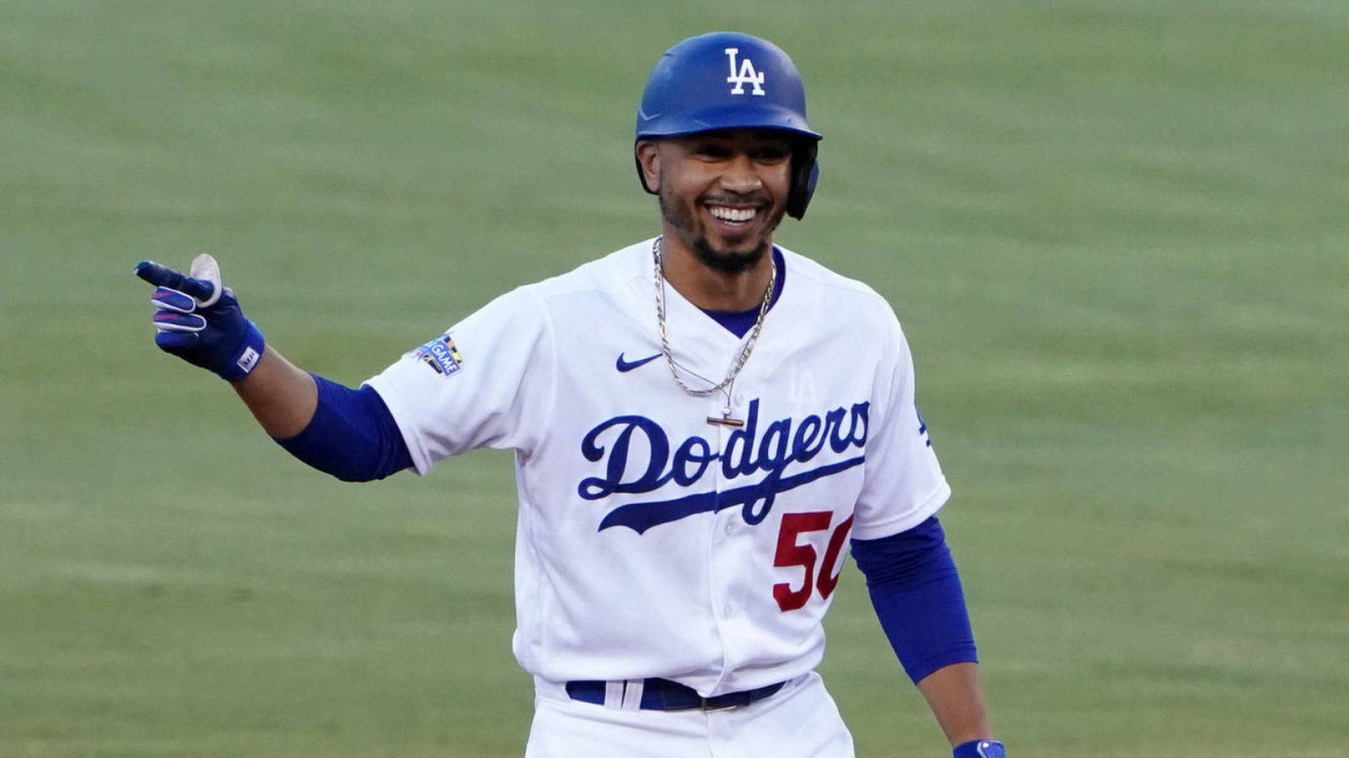 Mookie Betts 桌布 壁紙 — 一位身穿白色道奇隊棒球服的球員在綠色球場上戴著手套的手做手勢，露出燦爛的笑容。