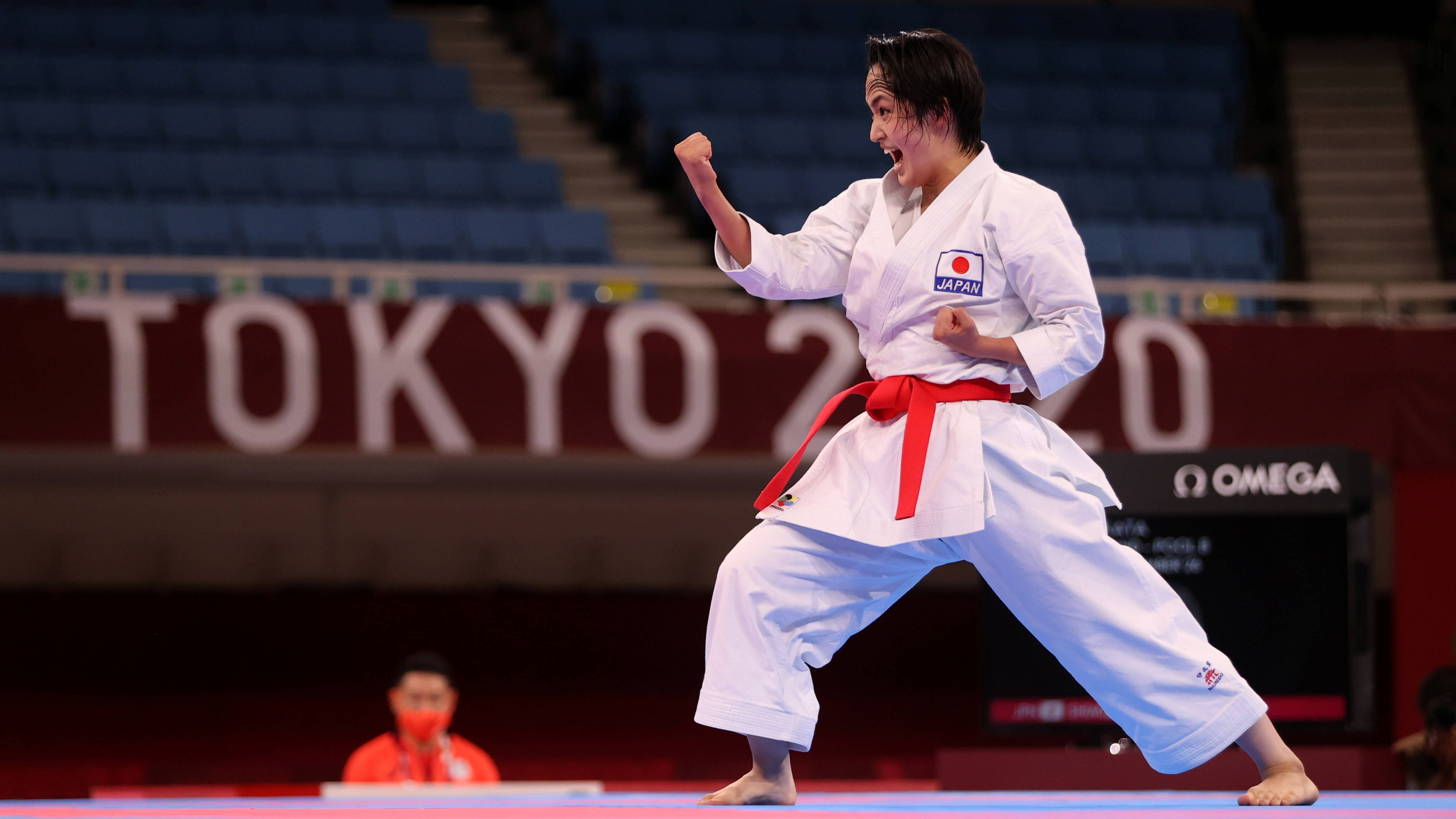 Athletic 桌布 壁紙 — 一位身穿白色道服、繫紅色腰帶的女空手道運動員在東京2020比賽期間於藍色軟墊上強力出擊。
