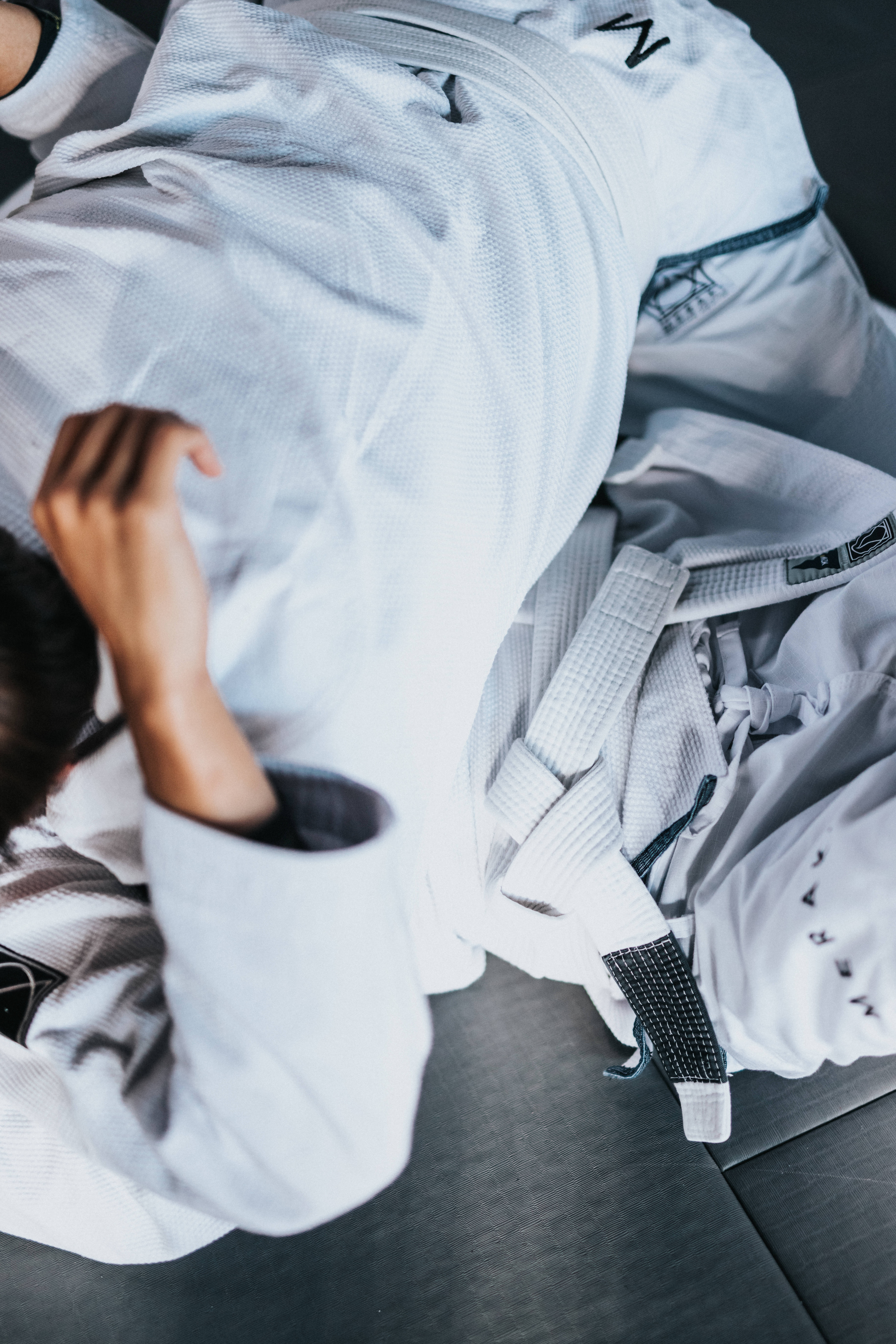 Judo 桌布 壁紙 — 一位身穿白色道服的武術家躺在黑暗的地板上，黑色腰帶部分可見，從高角度拍攝。