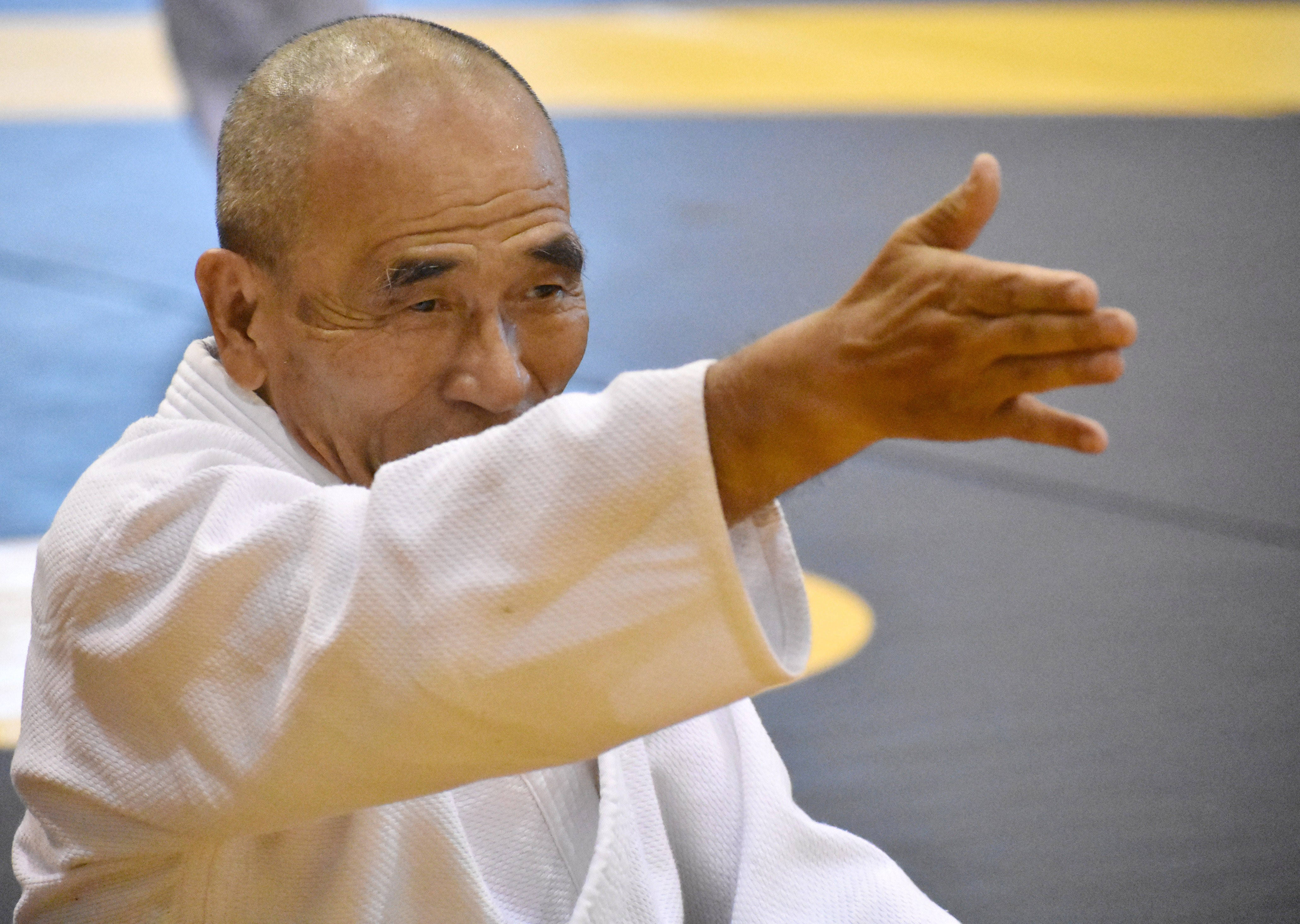martial arts 桌布 壁紙 — 一位身穿白色道服的長者武術家，在藍黃色軟墊上專注地伸出手。