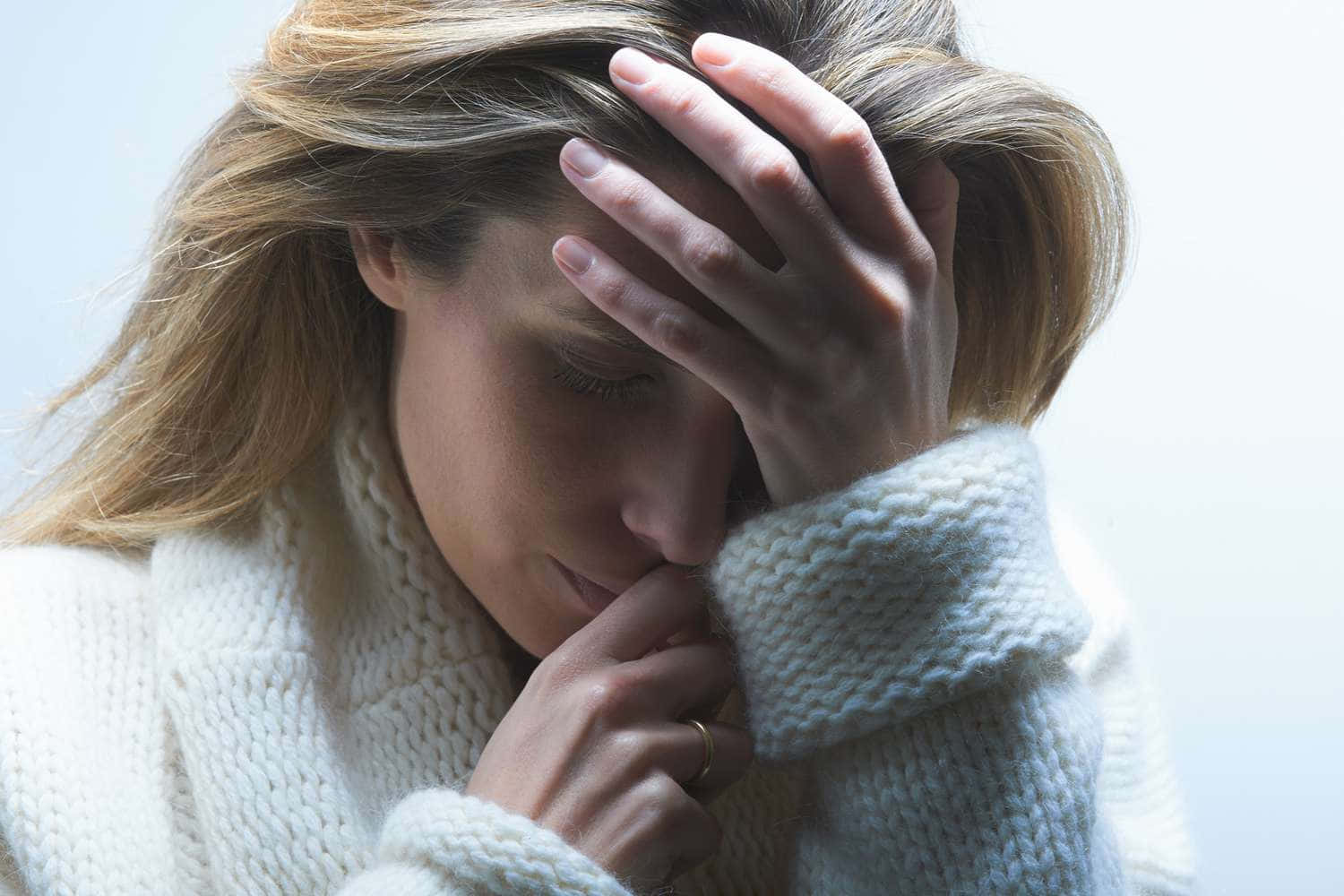Depressed 桌布 壁紙 — 一位身穿白色針織毛衣的女性，在純色背景下痛苦地閉著眼睛，用手托著頭。