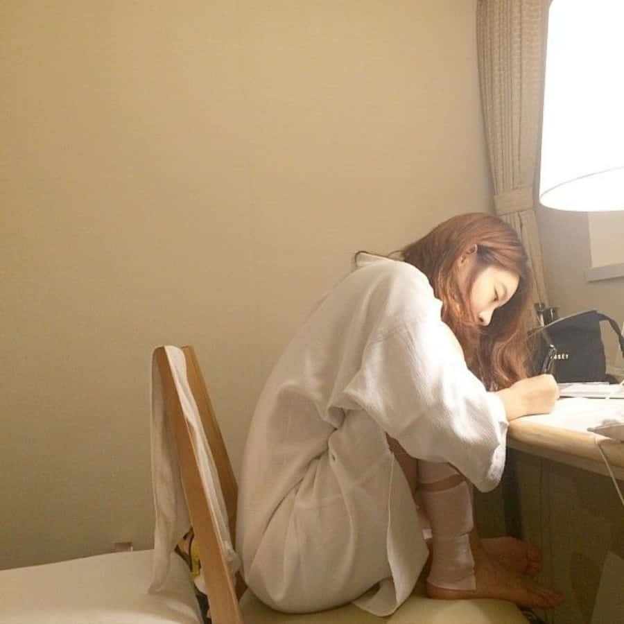 Study Aesthetic 桌布 壁紙 — 一位身穿白色長袍的年輕女子坐在燈光柔和的房間裡，彎腰伏案，專注地在燈下寫字。