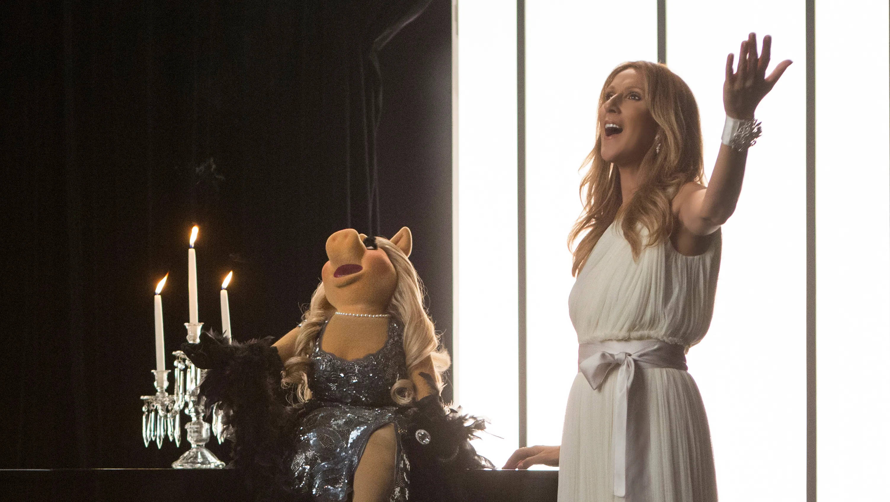 muppets 桌布 壁紙 — 一位身穿白色長裙的女性，在閃閃發光的銀色連衣裙的豬小姐旁邊，在點燃的蠟燭旁快樂地唱歌。
