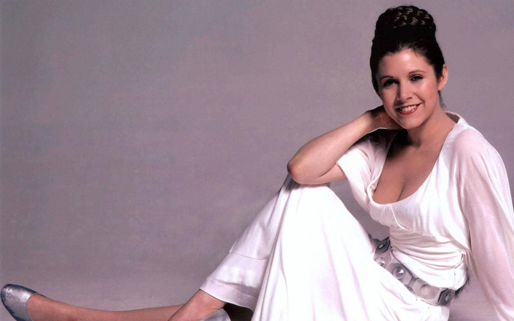 princess leia 桌布 壁紙 — 一位身穿白色長裙的女性坐在純灰色背景前微笑。