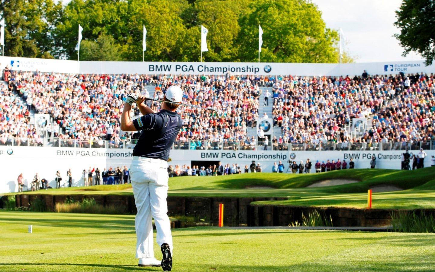 Pga 桌布 壁紙 — 一位身穿白色長褲和帽子的高爾夫球手在陽光明媚的綠色球場上揮桿，身後是座無虛席的觀眾看台。