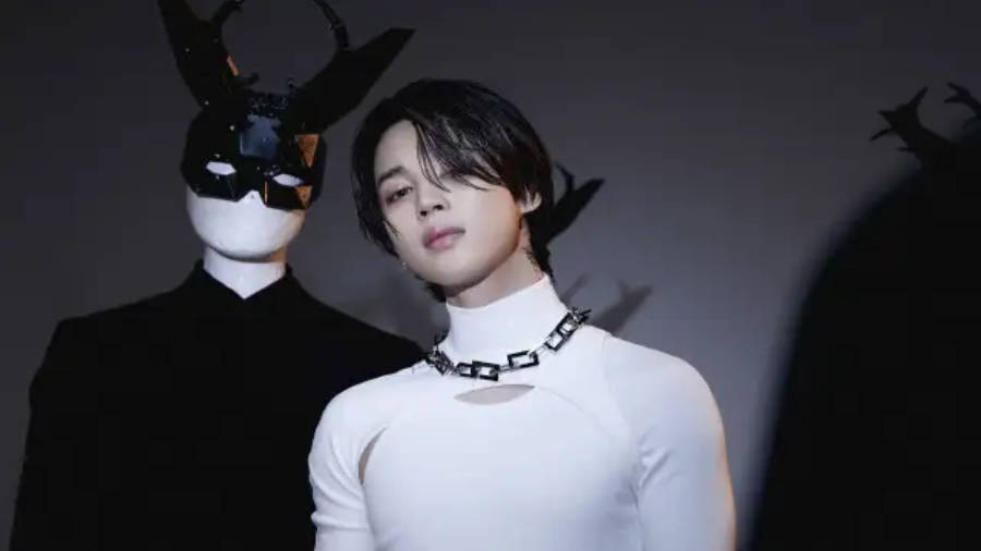 BTS 智旻 桌布 壁紙 — 一位身穿白色高領服裝的年輕男子，站在一個戴著面具、頭上有鹿角的角色旁邊，背景是深色攝影棚。