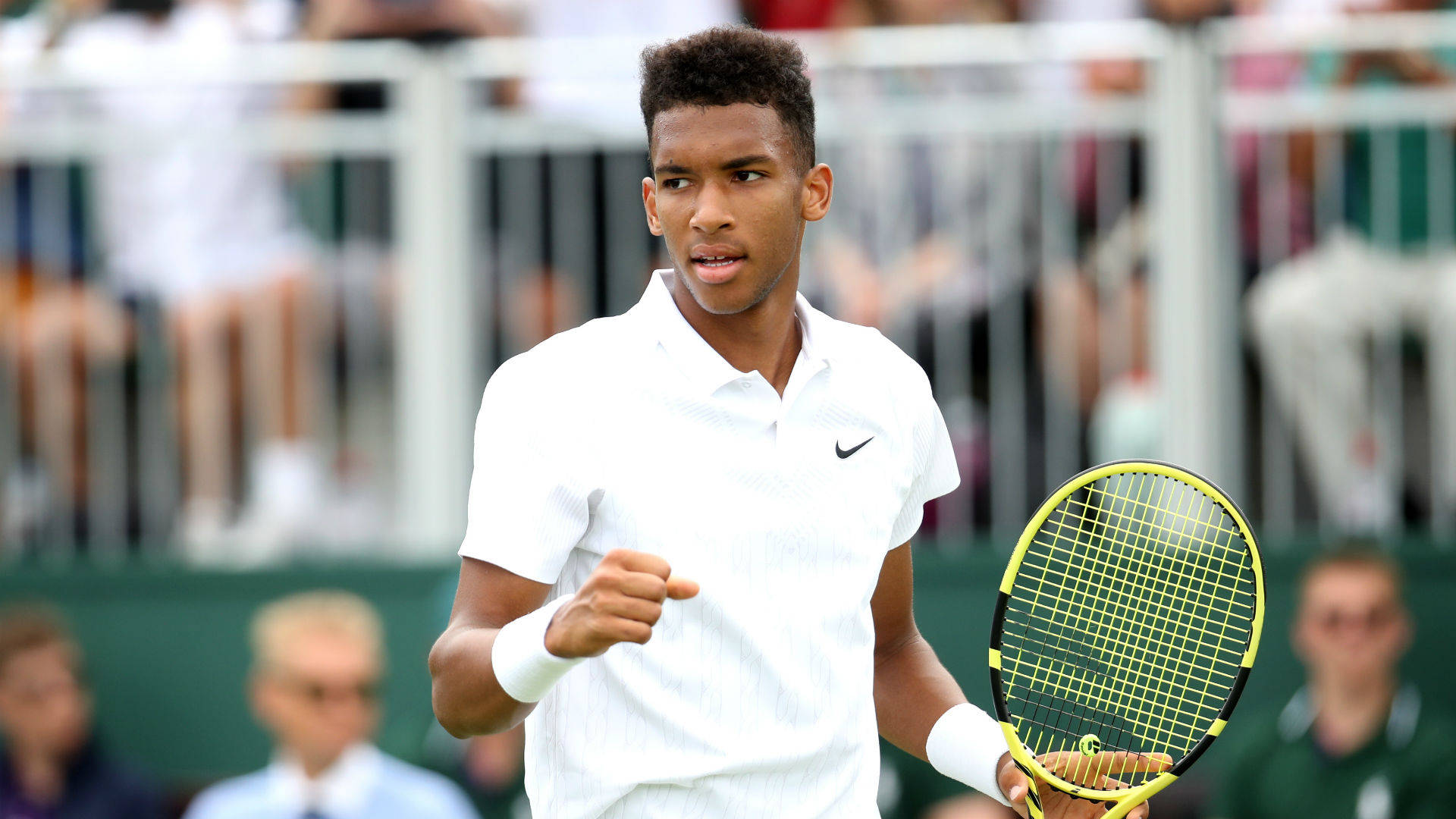 felix auger aliassime 桌布 壁紙 — 一位身穿白衫的年輕網球選手在草地場上握拳慶祝勝利，背景有觀眾。
