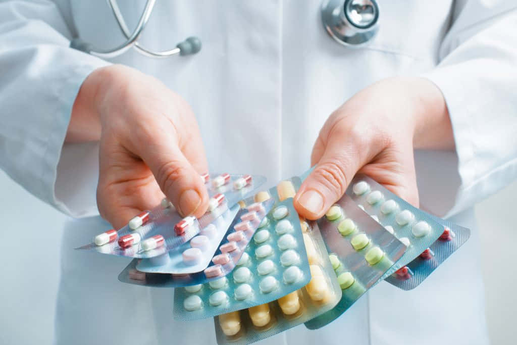 pills 桌布 壁紙 — 一位身穿白袍的醫生手持多個裝有彩色藥丸和膠囊的泡殼包裝。