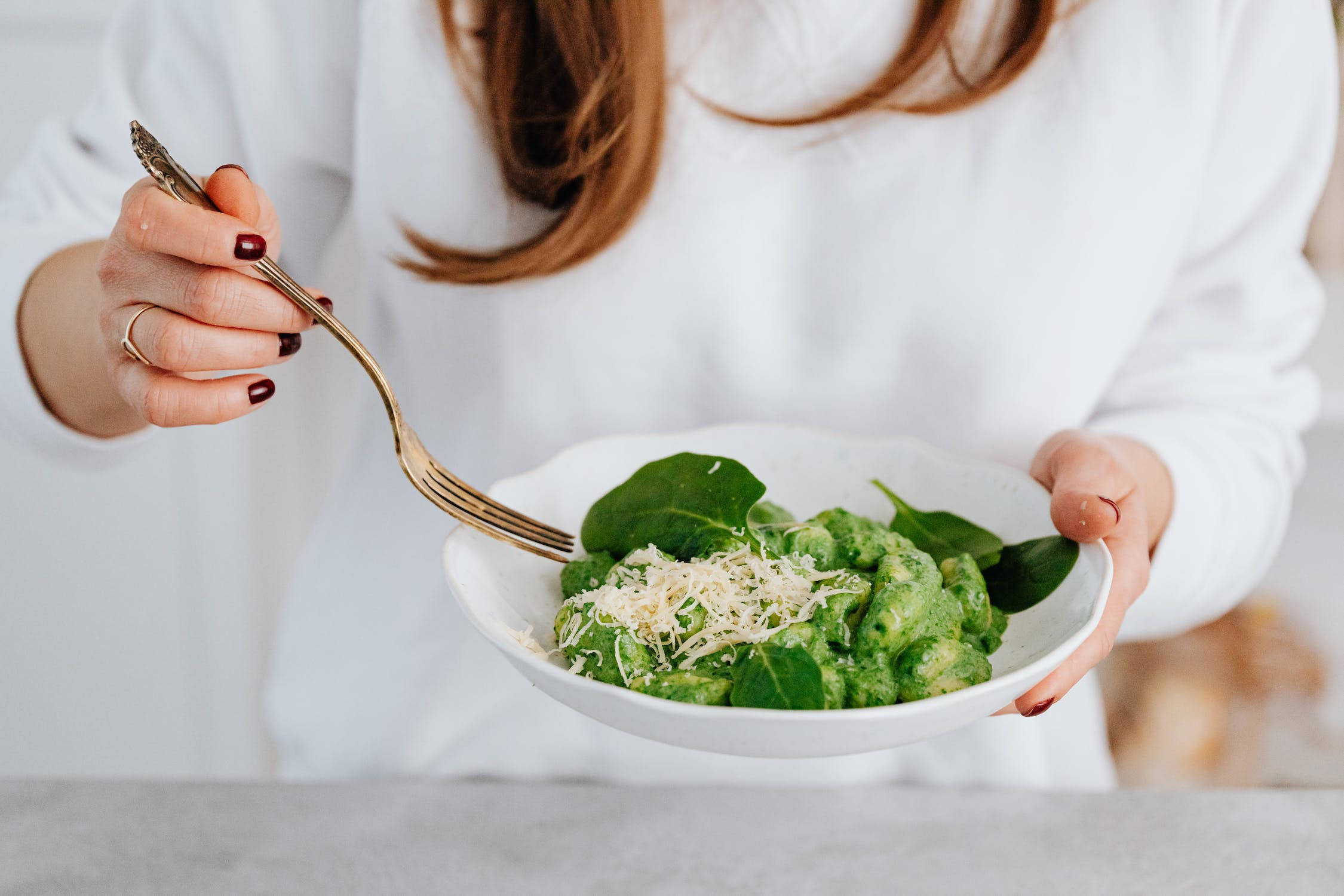 Healthy Food 桌布 壁紙 — 一位身穿白襯衫的人捧著一碗鮮綠色的義大利麵，上面鋪滿新鮮菠菜和磨碎的起司，準備進食。