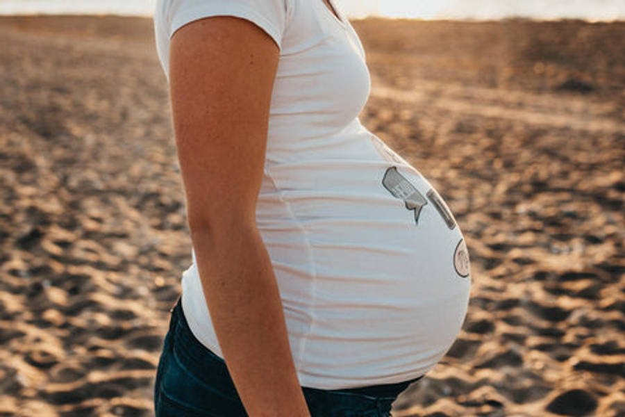 Pregnant 桌布 壁紙 — 一位身穿白襯衫的孕婦站在陽光普照的沙灘上，散發著溫暖的金色光芒。
