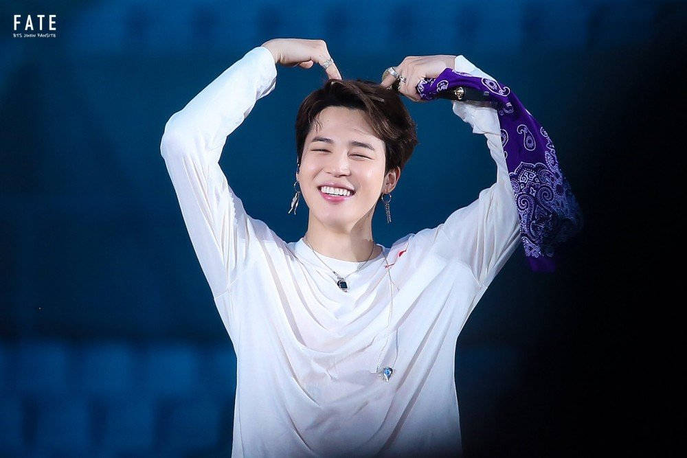 BTS 智旻 桌布 壁紙 — 一位身穿白襯衫的快樂表演者在藍色舞台燈光下，雙手在頭頂比出心形，露出燦爛笑容。