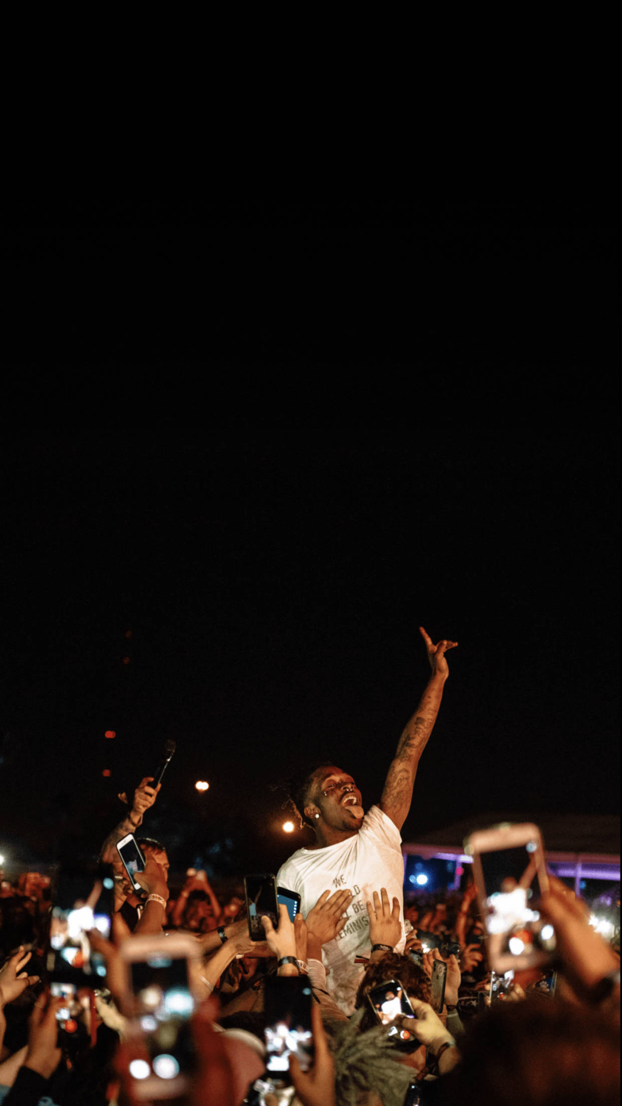 Rap Aesthetic 桌布 壁紙 — 一位身穿白襯衫的表演者在夜晚高舉一隻手臂，勝利的姿態高於一群舉著發光手機的粉絲。
