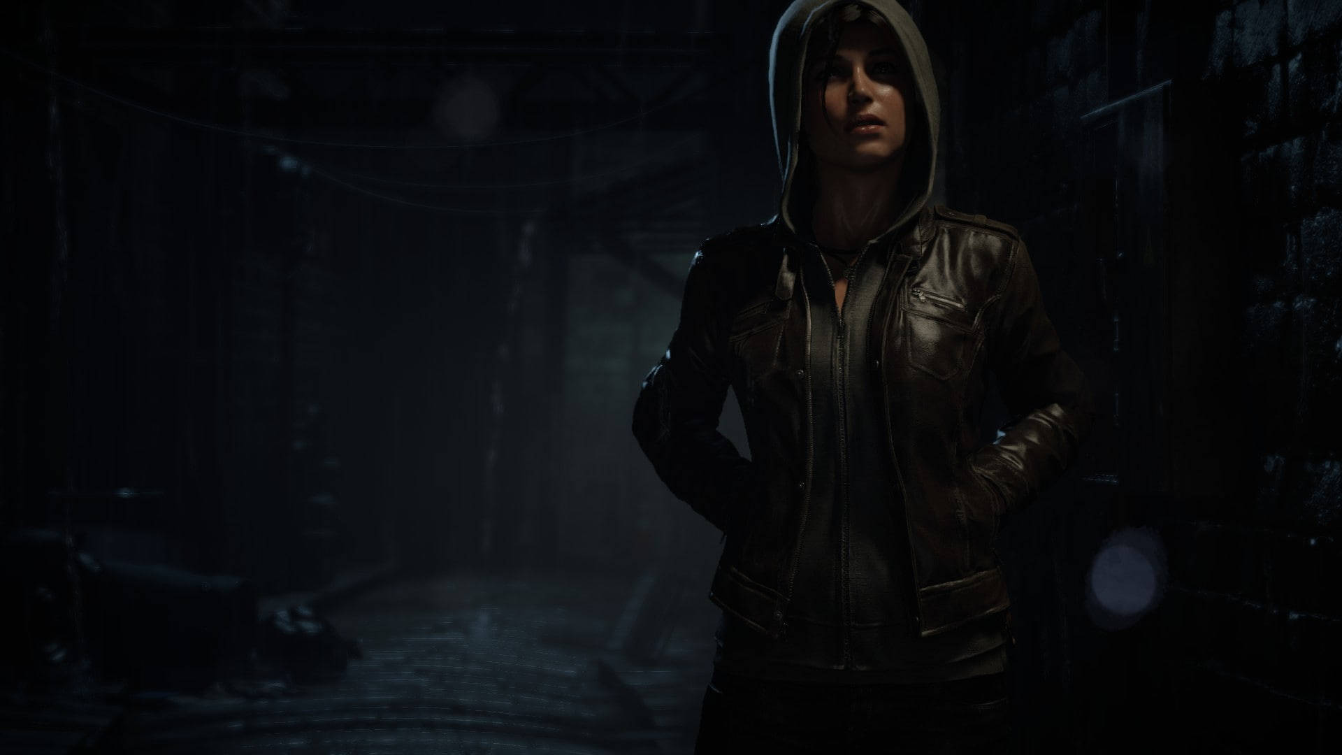 Rise Of The Tomb Raider 桌布 壁紙 — 一位身穿皮夾克、戴著連帽的女子，站在昏暗有霧的後巷，四周是磚牆和懸掛的電線。