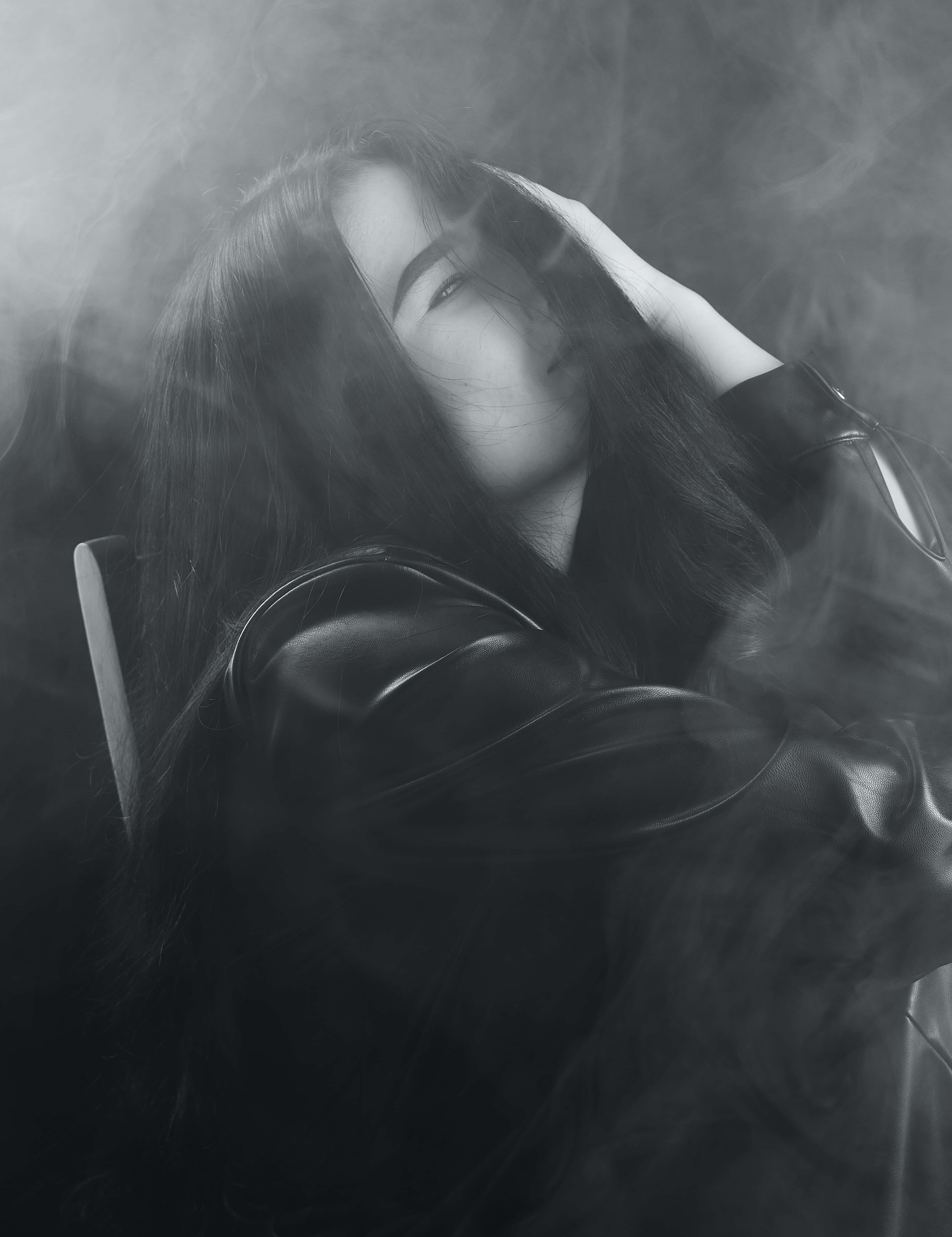 Black Smoke 桌布 壁紙 — 一位身穿皮夾克的女性在煙霧繚繞中將頭靠在手上，呈現出充滿氛圍的黑白肖像。