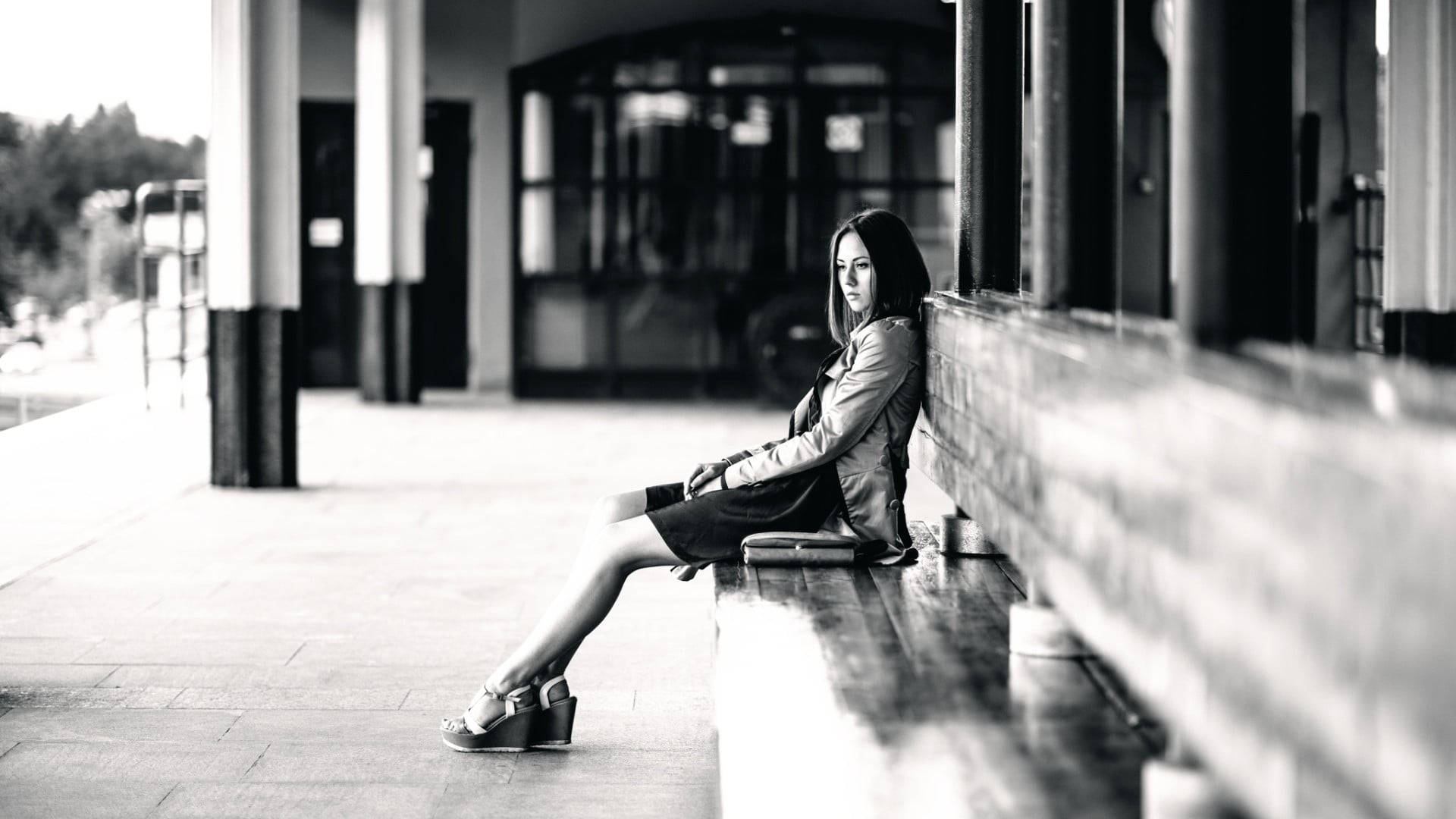 Alone 桌布 壁紙 — 一位身穿皮夾克的女性獨自坐在有蓋走道下的長椅上，黑白畫面，若有所思。