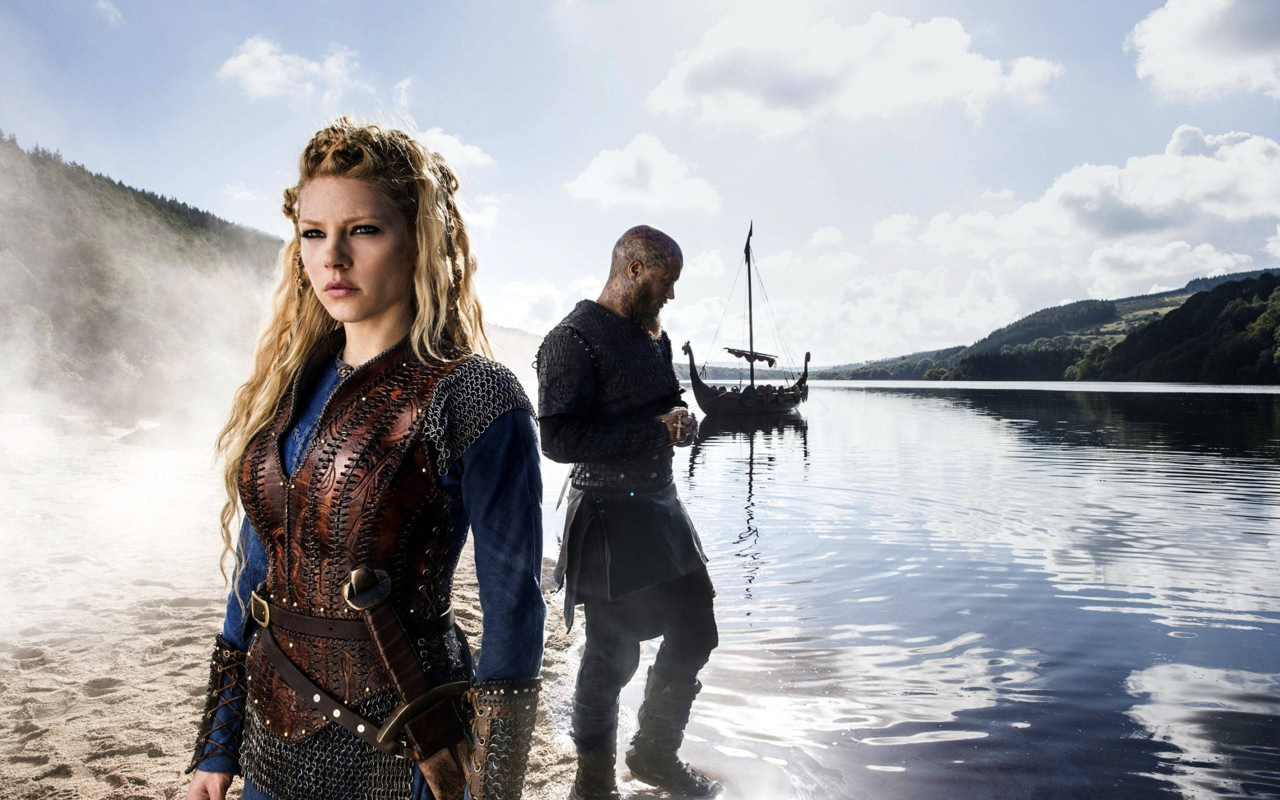 Vikings 桌布 壁紙 — 一位身穿皮甲的女維京人站在霧氣瀰漫的湖岸邊，一名男子正走向水中的長船。