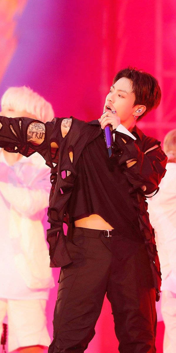 Jungkook 桌布 壁紙 — 一位身穿破爛黑色服裝的男表演者在充滿活力的粉紅色舞台燈光下，熱情地對著紫色麥克風唱歌。