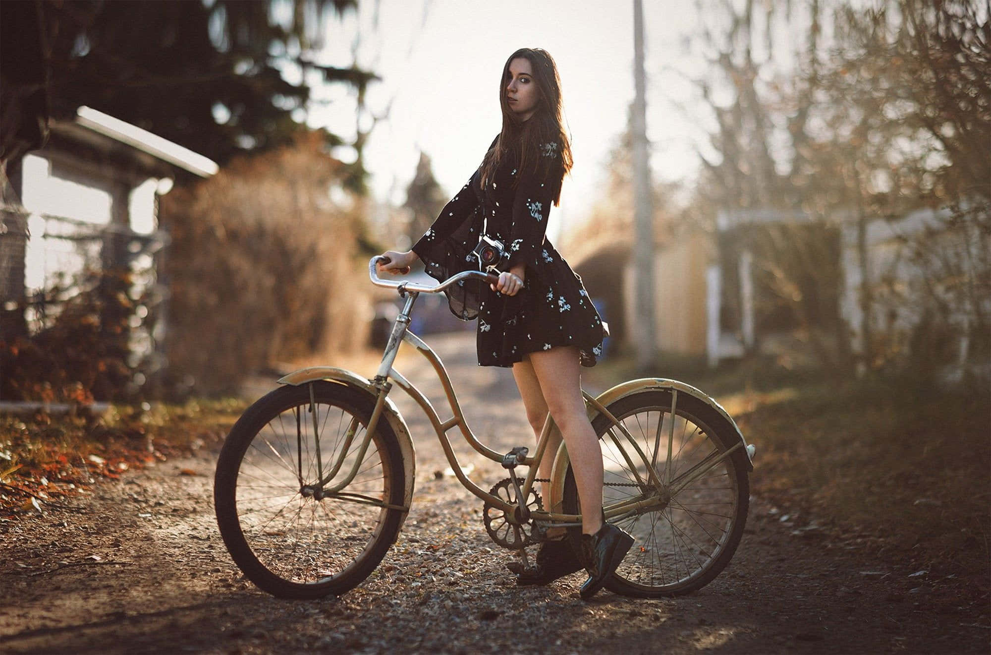 Beach Cruiser 桌布 壁紙 — 一位身穿碎花裙的年輕女子站在一條陽光明媚的泥土小徑上，旁邊是一輛復古腳踏車，四周環繞著秋天的樹木。