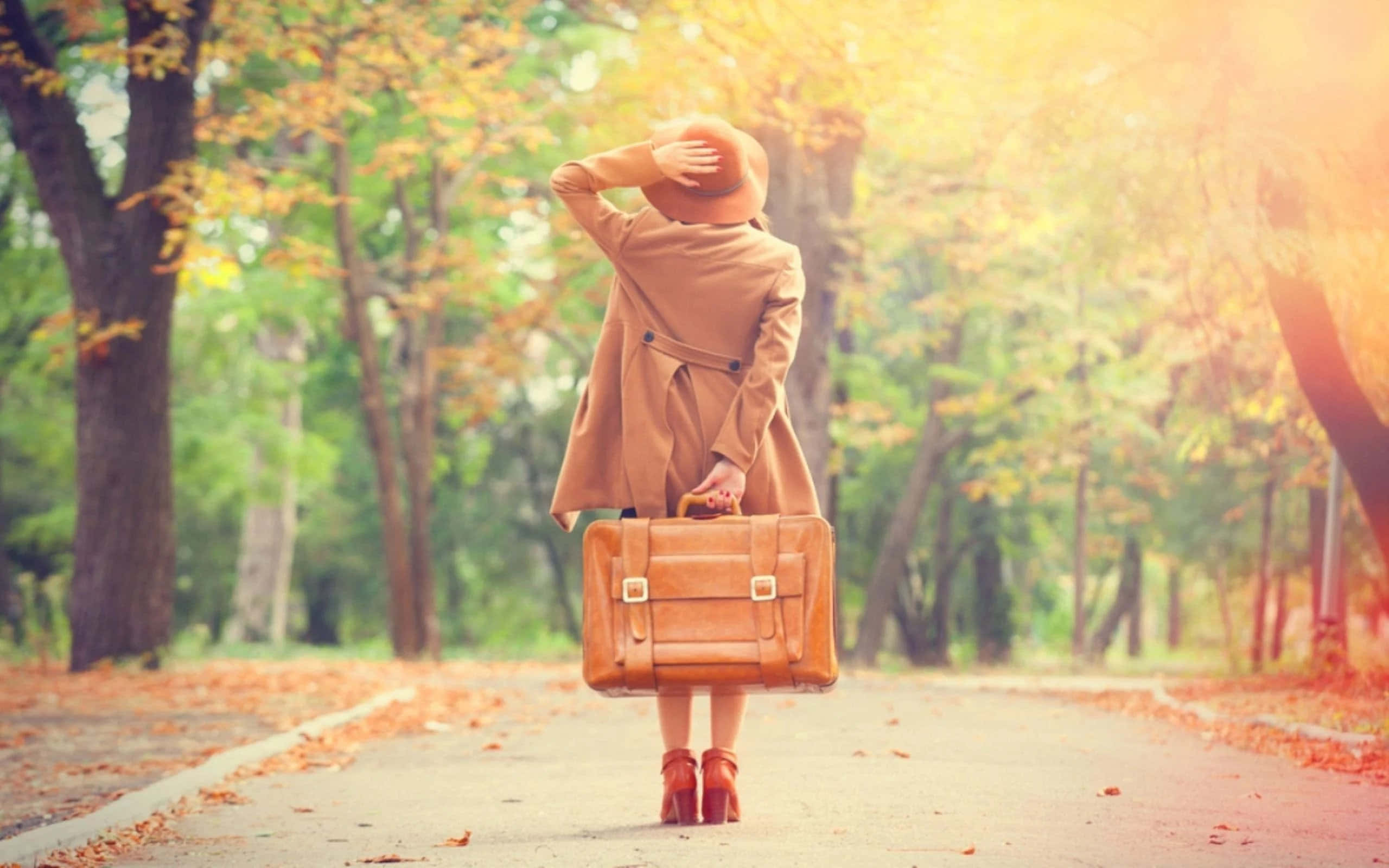 Vacation 桌布 壁紙 — 一位身穿米色外套和帽子的女士，在秋天落葉滿佈的小徑上行走，手提復古行李箱，遮擋陽光。
