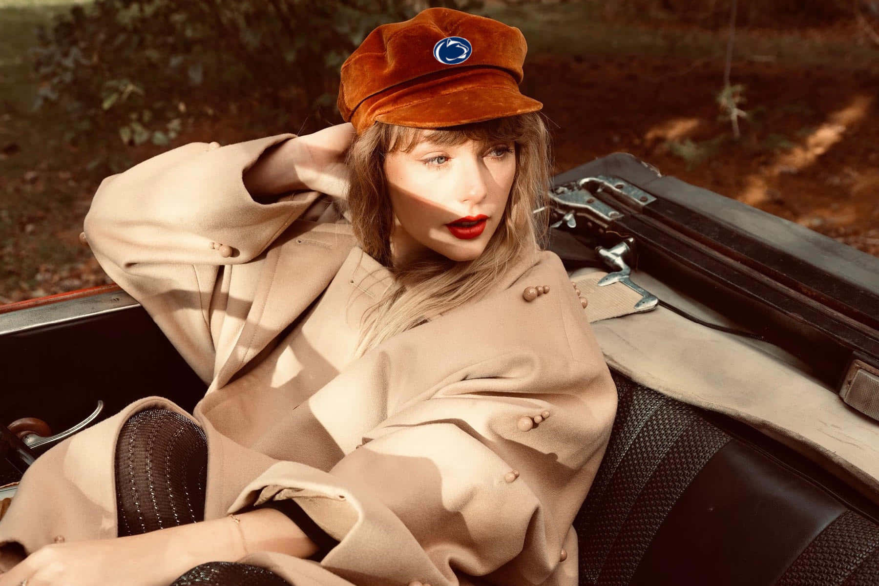 Taylor Swift Laptop 桌布 壁紙 — 一位身穿米色外套和棕色帽子的女士，在溫暖的金色陽光穿過樹林灑落時，於一輛復古車中悠閒地休息。