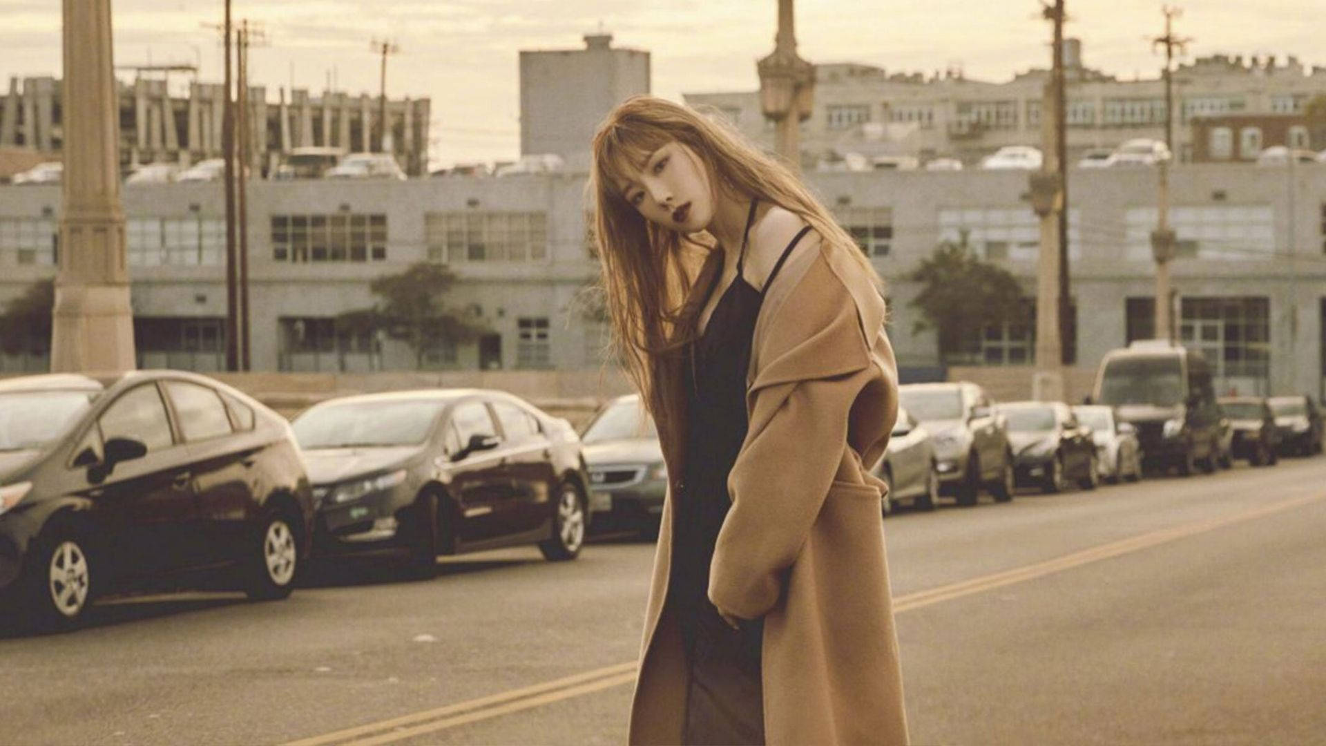 태연 桌布 壁紙 — 一位身穿米色外套的年輕女子，在停滿汽車的城市街道上，在朦朧的金色天空下若有所思地站著。