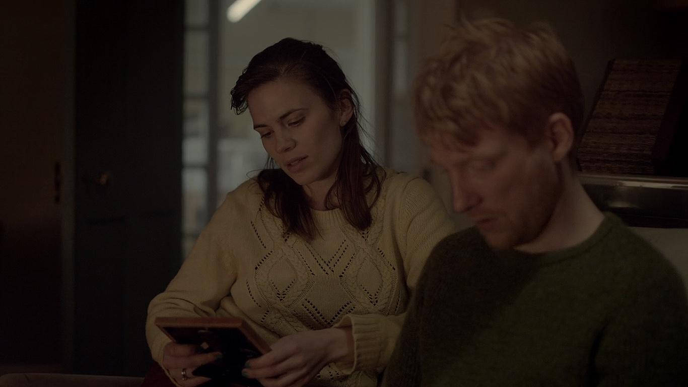 Netflix 桌布 壁紙 — 一位身穿米色毛衣的女性專注地使用平板電腦，而一位身穿綠色毛衣的男性坐在她旁邊，房間光線昏暗。