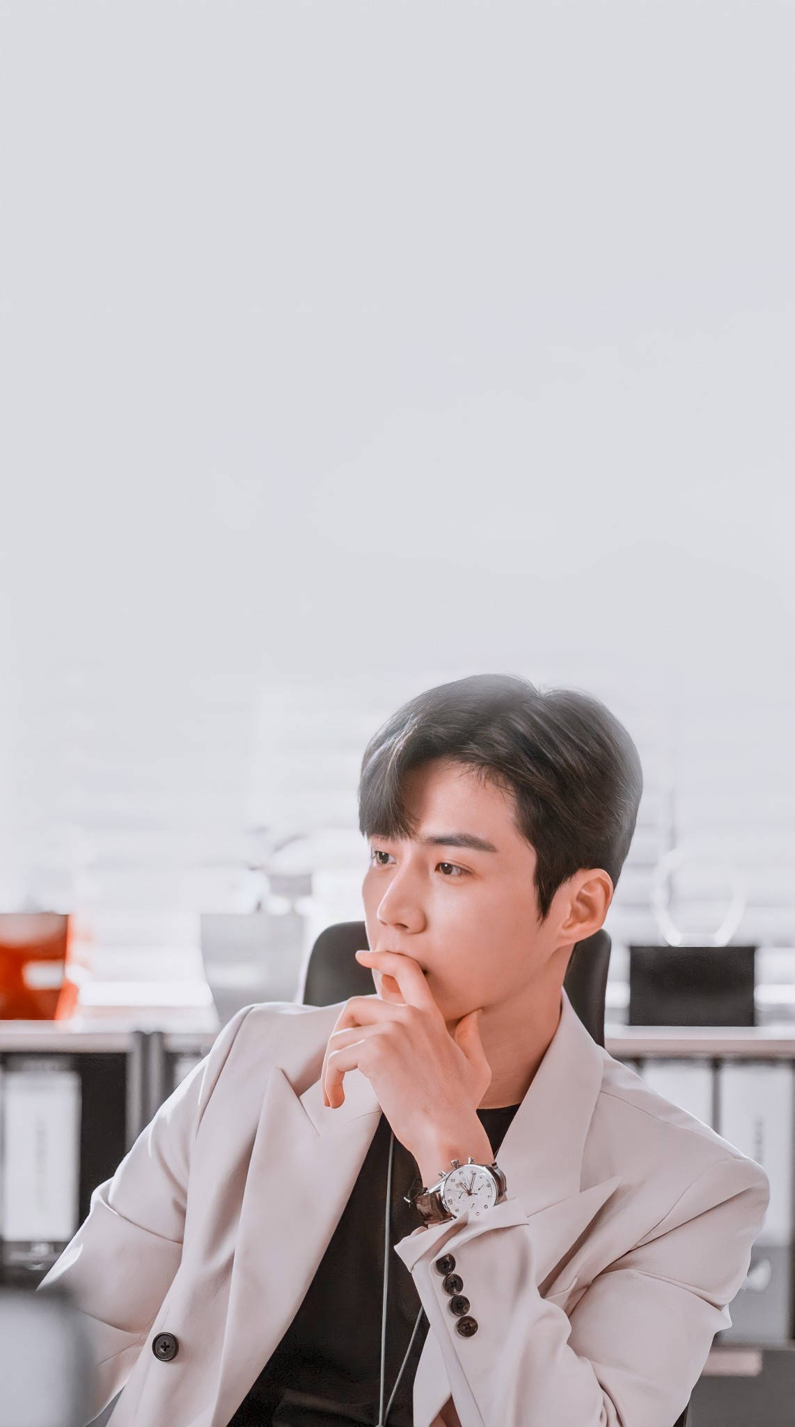 Kim Seon Ho 桌布 壁紙 — 一位身穿米色西裝外套的年輕男子在簡約風格的辦公室裡托腮沉思。