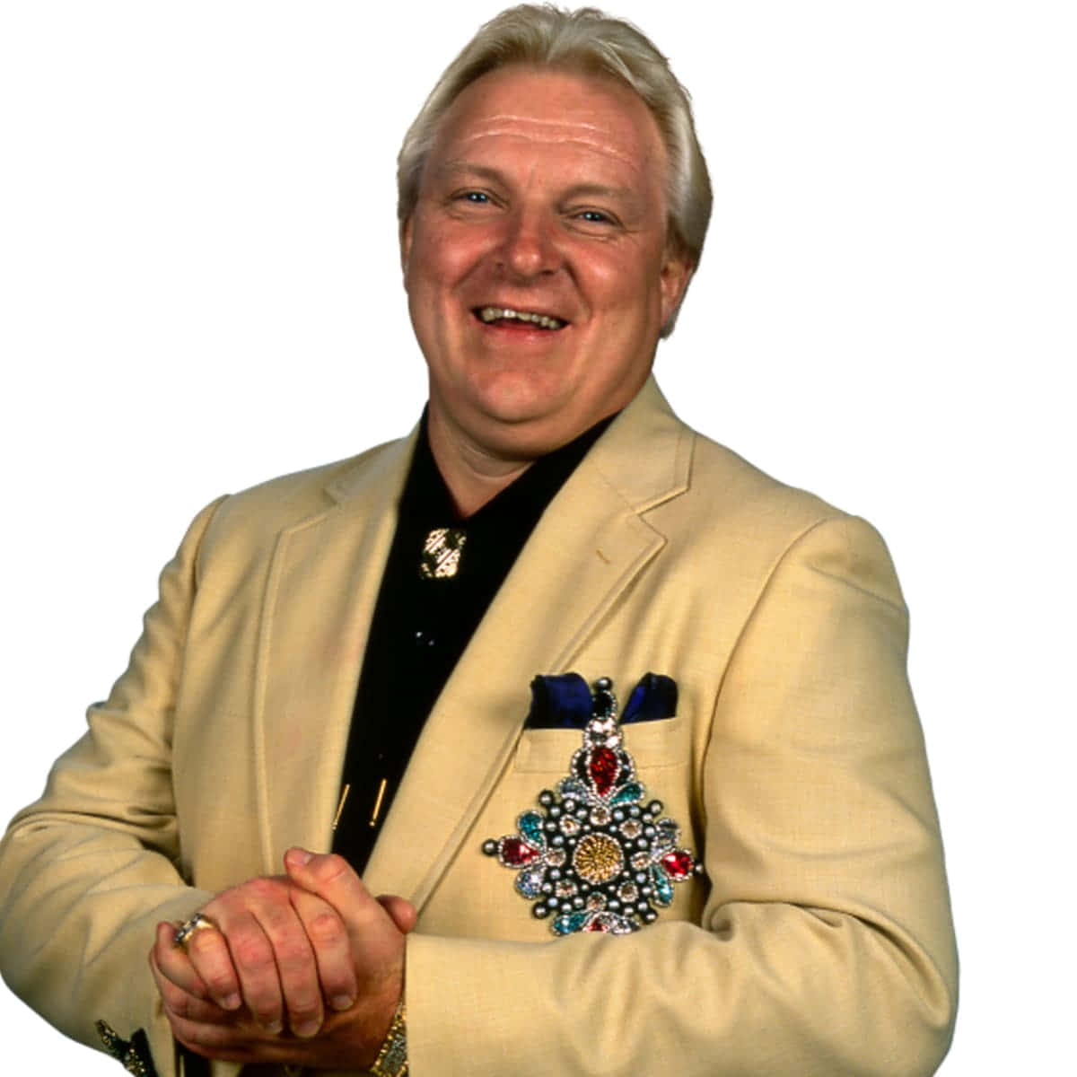 Bobby Heenan 桌布 壁紙 — 一位身穿米色西裝的開朗男士微笑著，胸前佩戴著一枚色彩繽紛的珠寶獎章。