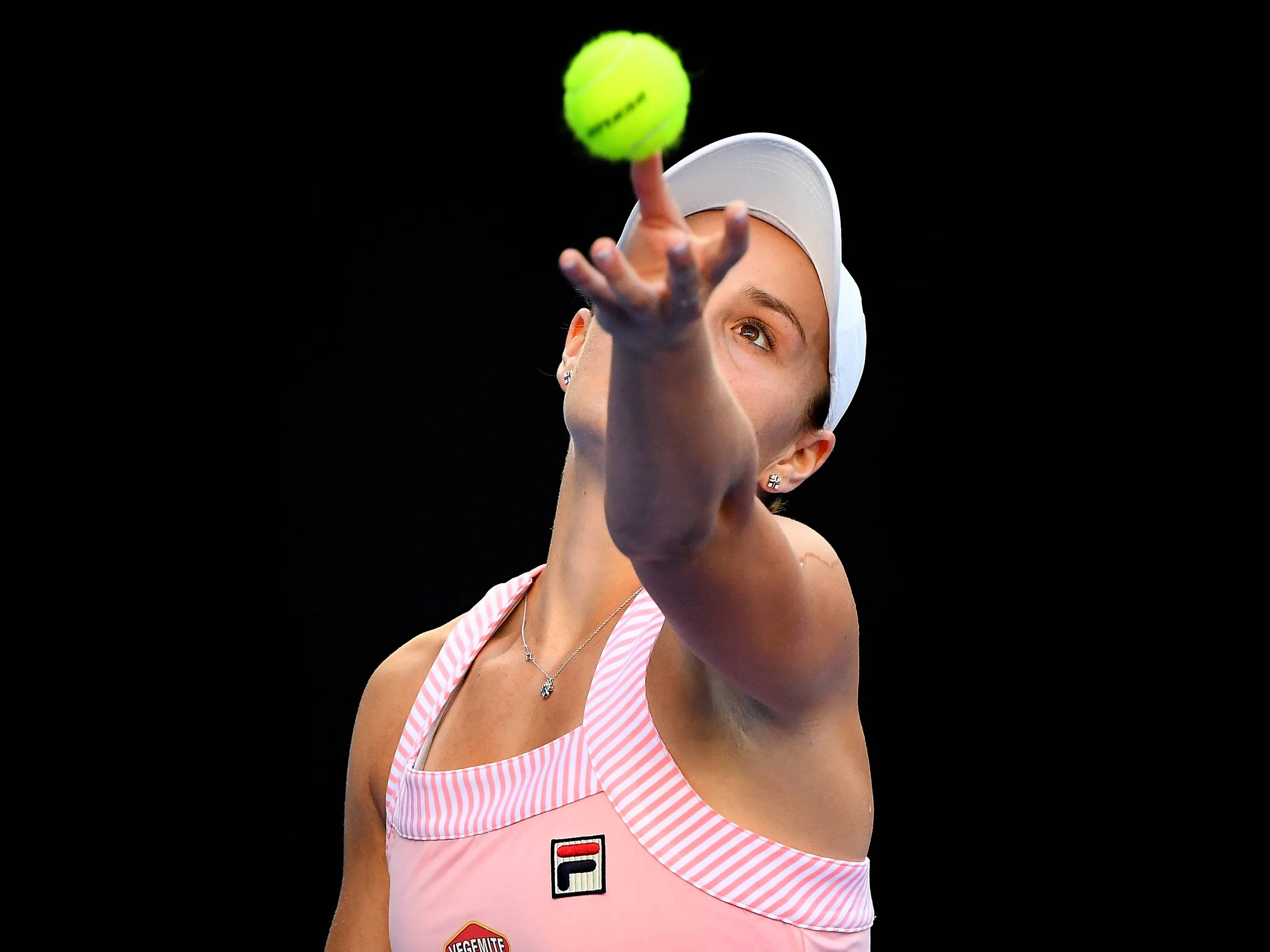 Ashleigh Barty 桌布 壁紙 — 一位身穿粉紅條紋上衣的女網球選手，在純黑色背景前拋起一顆亮黃色的網球。