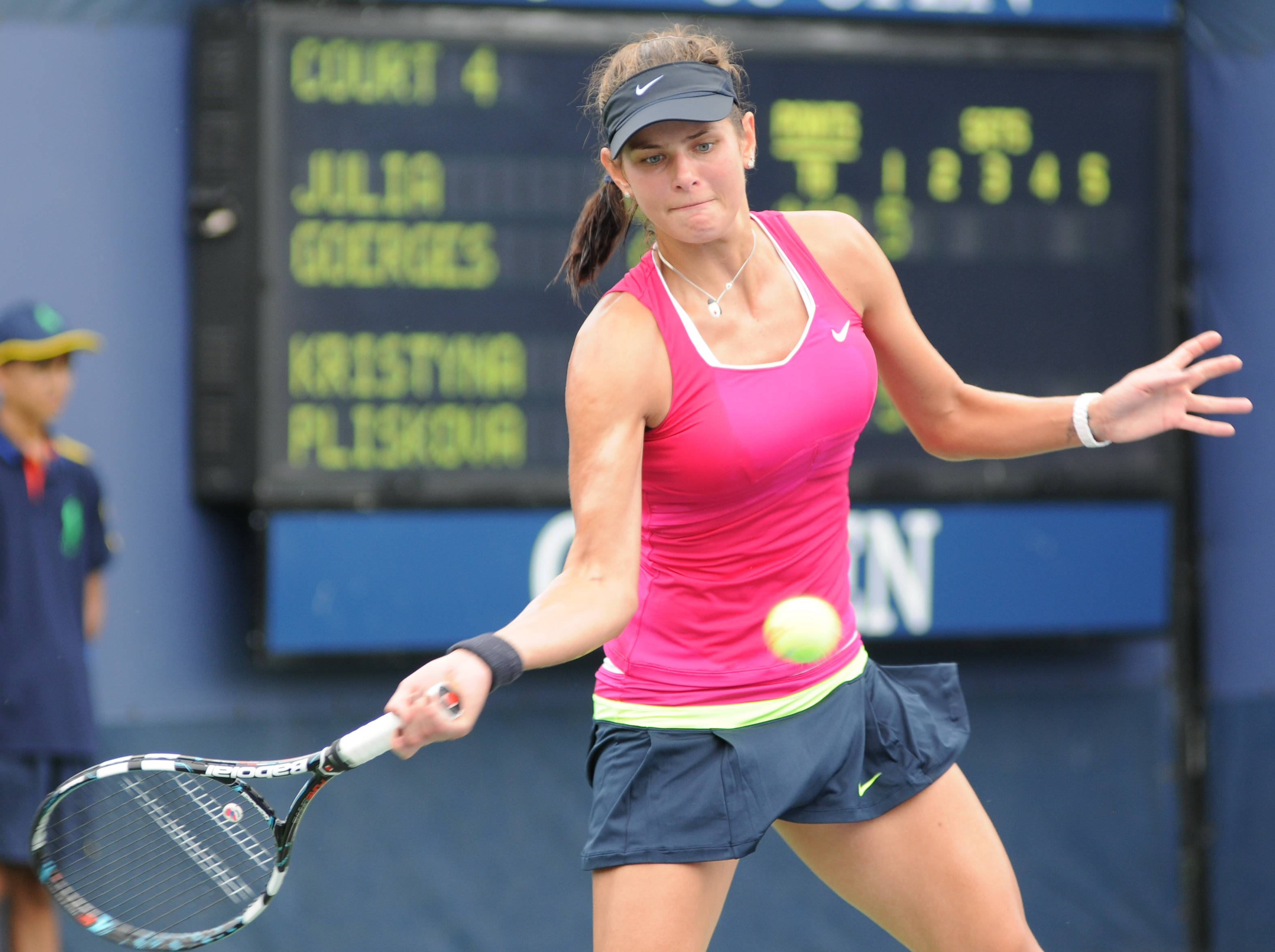 Tennis 桌布 壁紙 — 一位身穿粉紅色上衣和海軍藍短褲的女網球選手在4號球場比賽中揮拍擊打黃色網球。