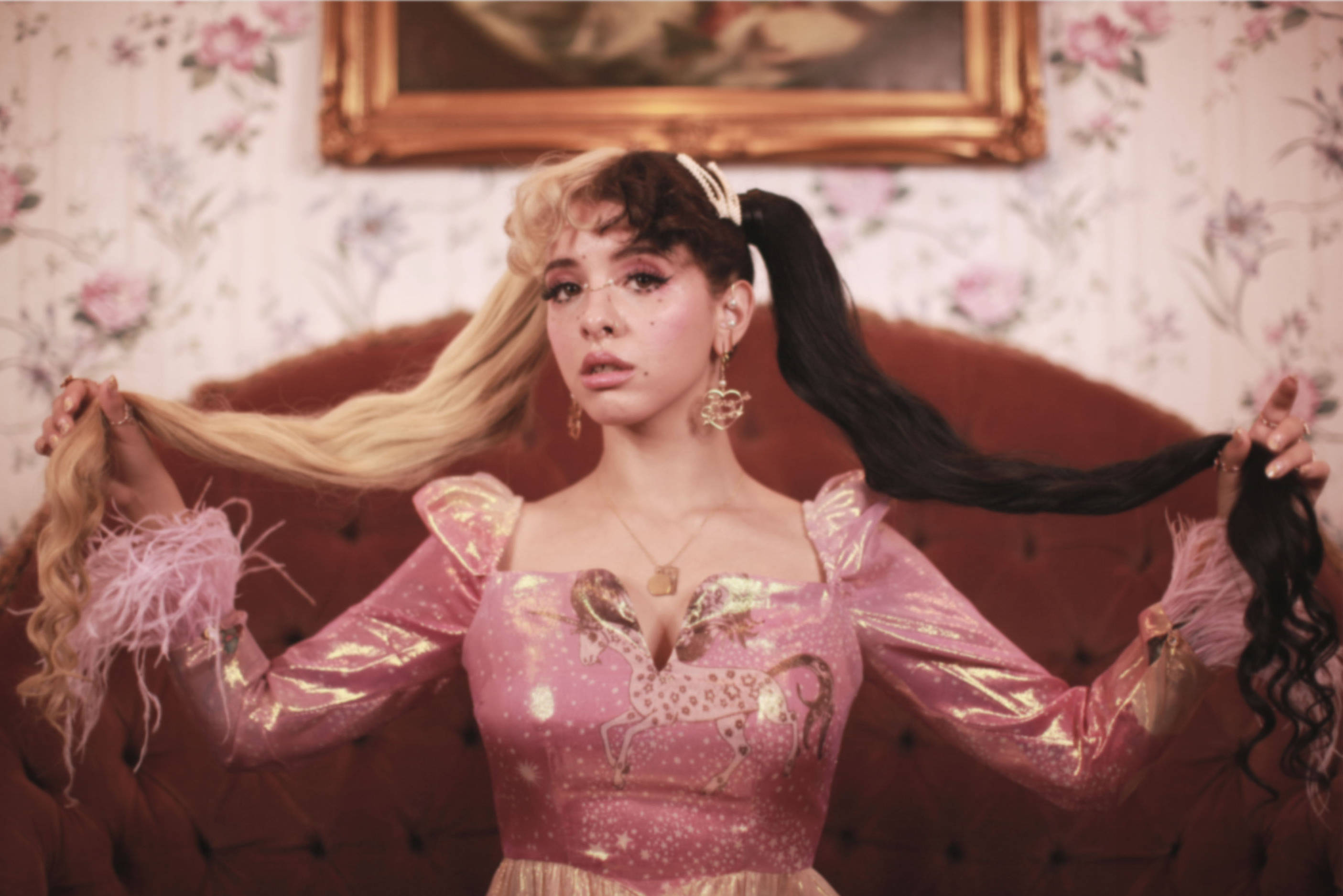 Melanie 桌布 壁紙 — 一位身穿粉紅色亮片連衣裙的女性，在花卉壁紙背景下，手持兩種對比鮮明的髮色，一頭金髮一頭黑髮。