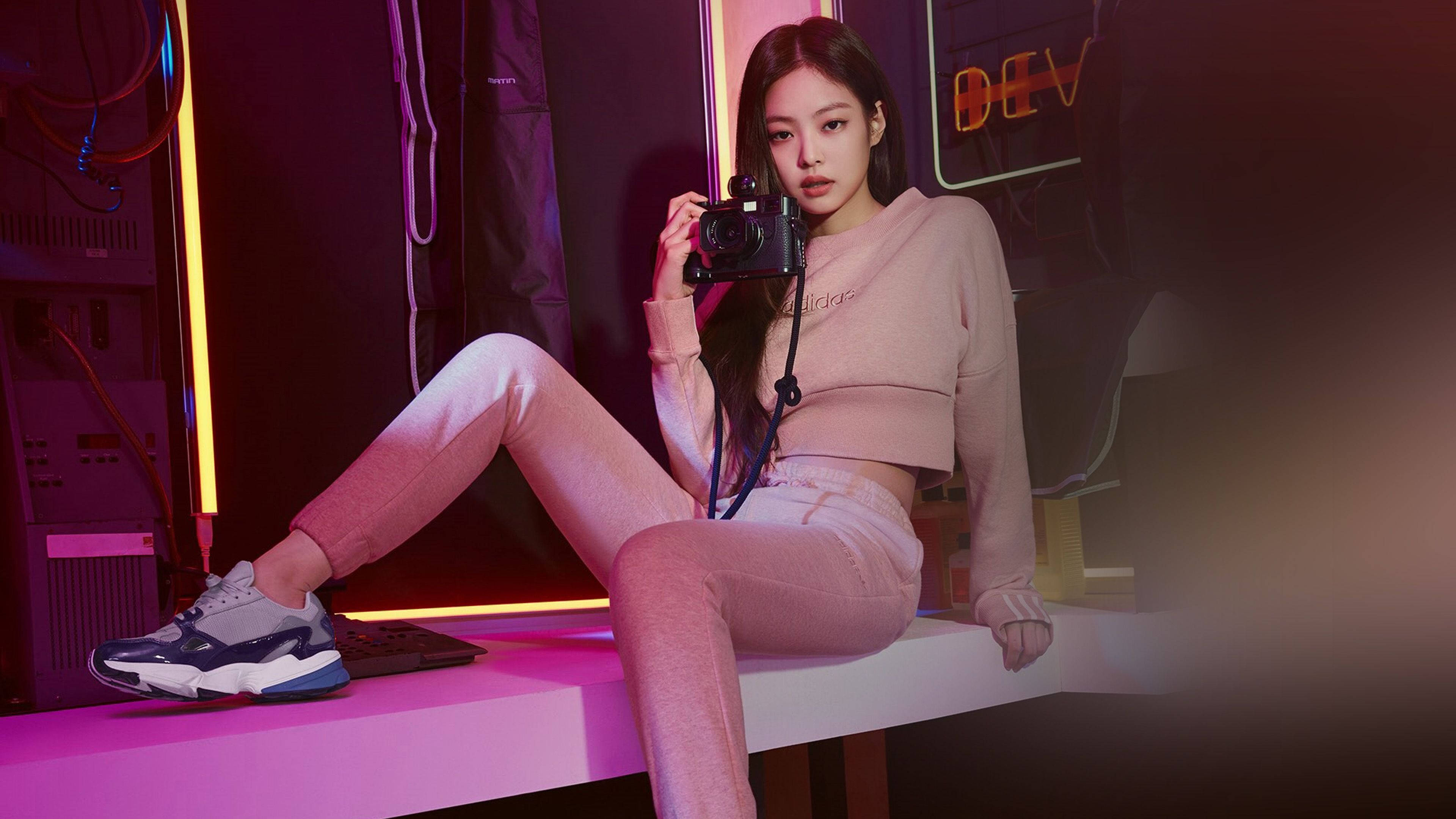 BLACKPINK 桌布 壁紙 — 一位身穿粉紅色休閒服的年輕女性坐在發光的粉紅色平台上，在霓虹燈照亮的科技室內拿著相機。