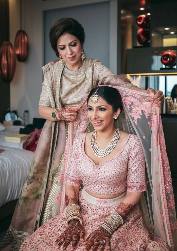 Wedding 桌布 壁紙 — 一位身穿粉紅色刺繡 lehenga 的新娘在現代飯店房間裡微笑，母親為她調整花紗。