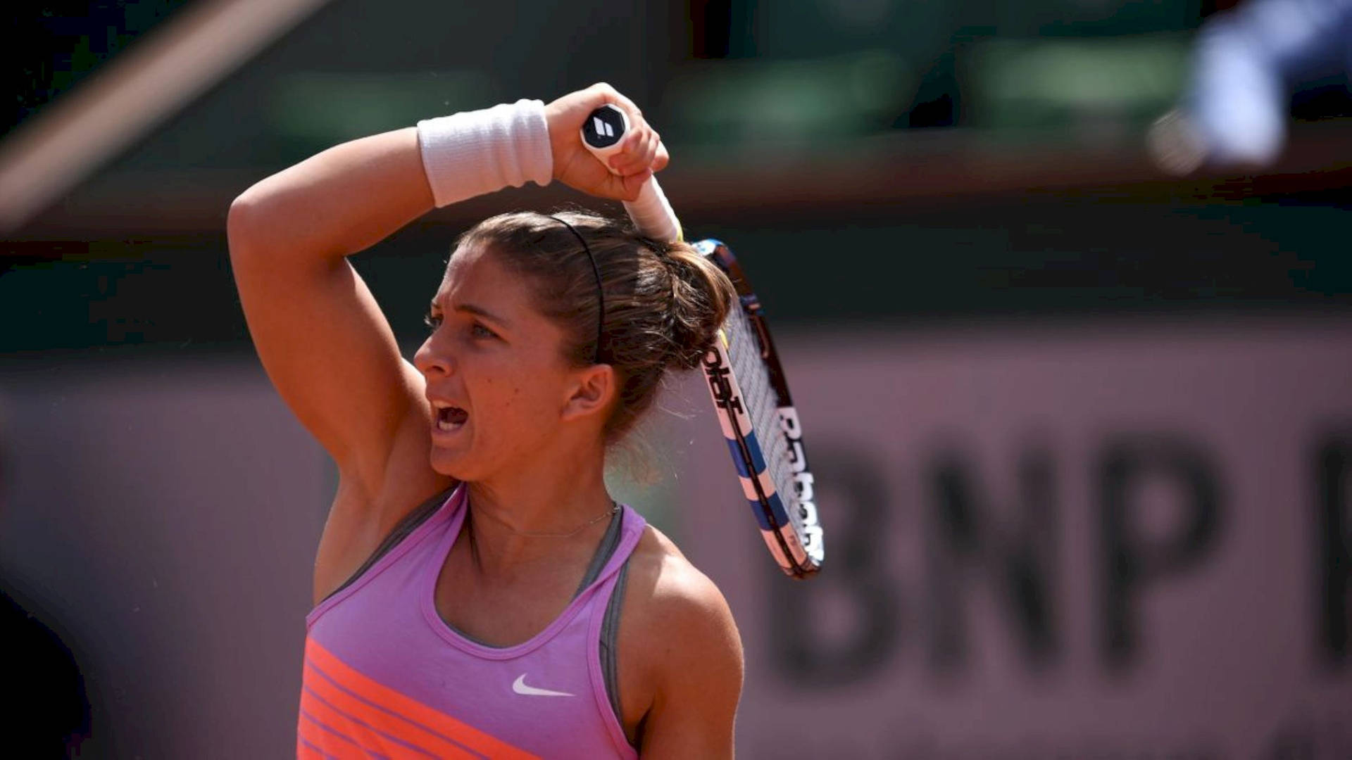 Nike 桌布 壁紙 — 一位身穿粉紅色和橙色球衣的女網球選手在紅土球場上揮拍時發出強烈的吼叫。