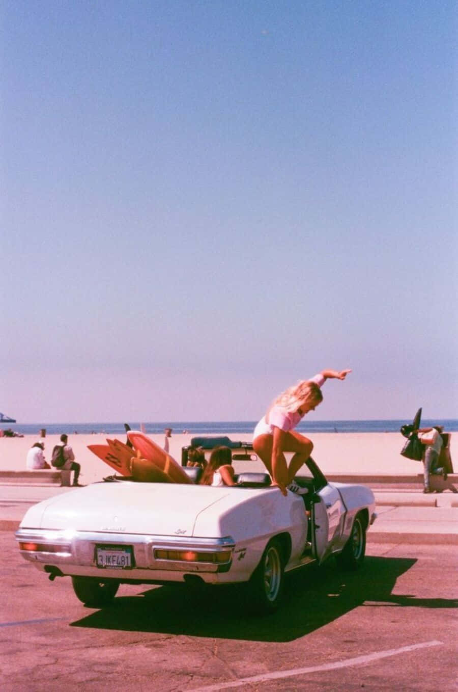90's Vintage Retro Aesthetic 桌布 壁紙 — 一位身穿粉紅色泳衣的女性在停泊於陽光明媚的海灘上的白色敞篷車上擺姿勢，背景可見衝浪板和海洋。