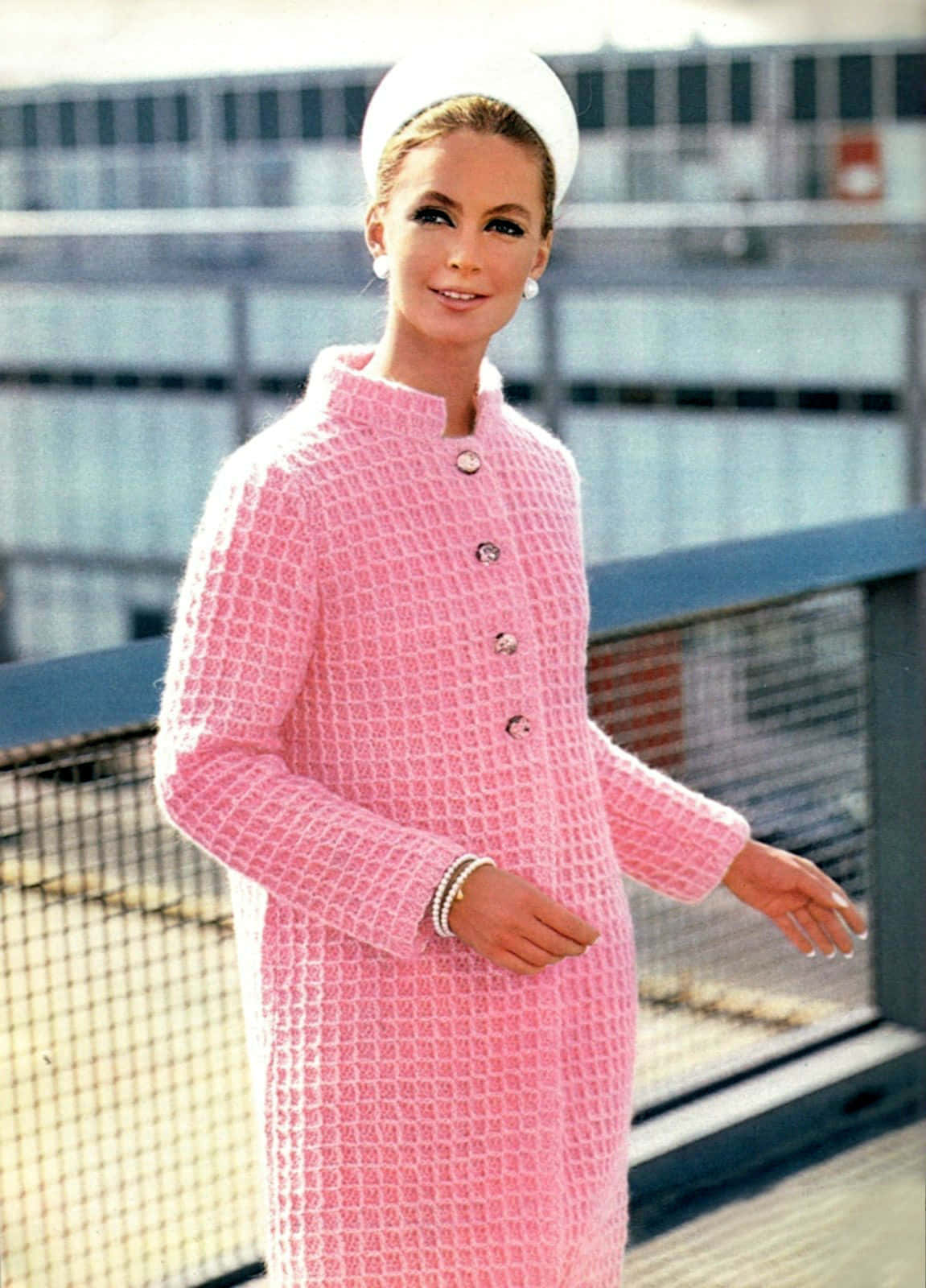 Pink Coat 桌布 壁紙 — 一位身穿粉紅色紋理外套和白色帽子的女士在現代陽台上微笑，陽台有玻璃欄杆。