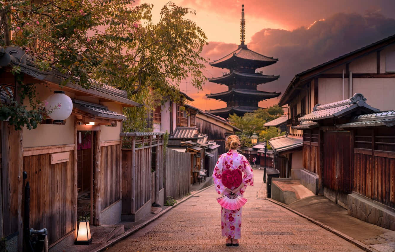 日本 桌布 壁紙 — 一位身穿粉紅色花卉和服的女士在日落時分沿著狹窄的日本街道走向寶塔。