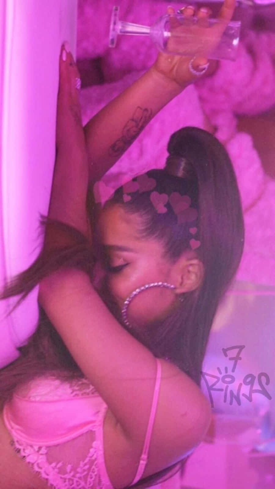 Ariana Grande 7 Rings 桌布 壁紙 — 一位身穿粉紅色蕾絲內衣的女性在豪華的粉紅色房間裡休息，手持一杯飲料，頭部附近漂浮著心形圖案。