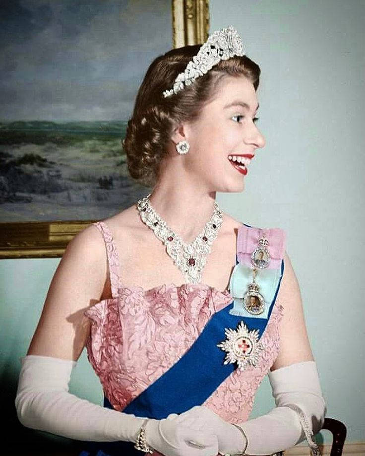 Queen Elizabeth 桌布 壁紙 — 一位身穿粉紅色蕾絲長袍的燦爛年輕女王，戴著鑽石頭飾項鍊和帶有獎章的藍色肩帶微笑。