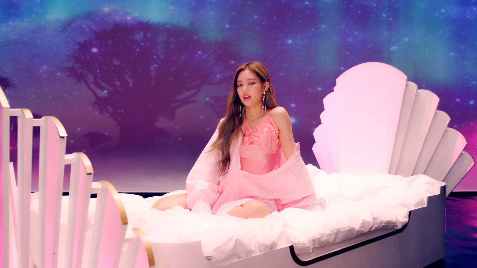 BLACKPINK 桌布 壁紙 — 一位身穿粉紅色衣服的女性坐在白色貝殼形床上，背景是繁星點點的紫色和藍色宇宙，有一棵剪影樹。