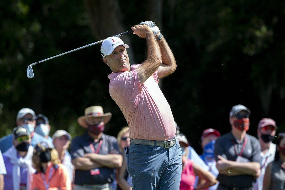 高爾夫 桌布 壁紙 — 一位身穿粉紅色襯衫的高爾夫球手在明亮的陽光下，在樹後觀眾的注視下，專注地揮桿。